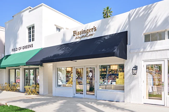 White storefront with green and navy awnings, Bissinger's signage, outdoor seating, and palm trees