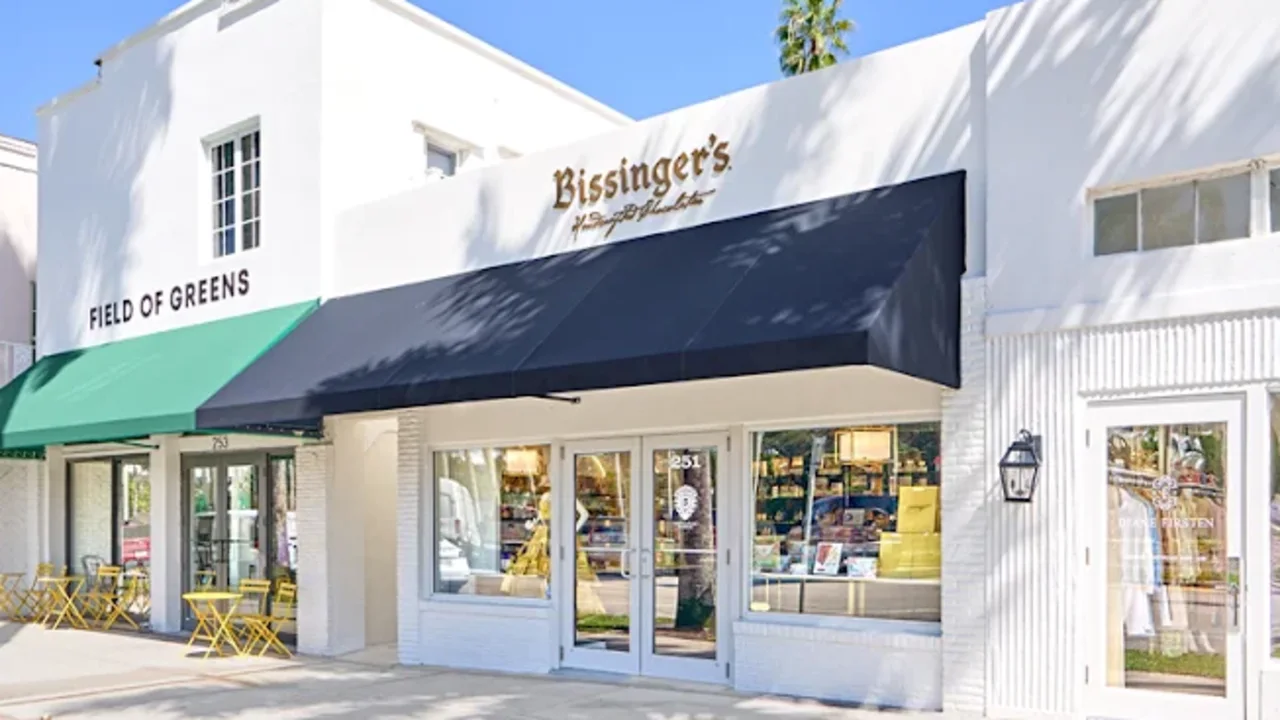 White storefront with green and navy awnings, Bissinger's signage, outdoor seating, and palm trees