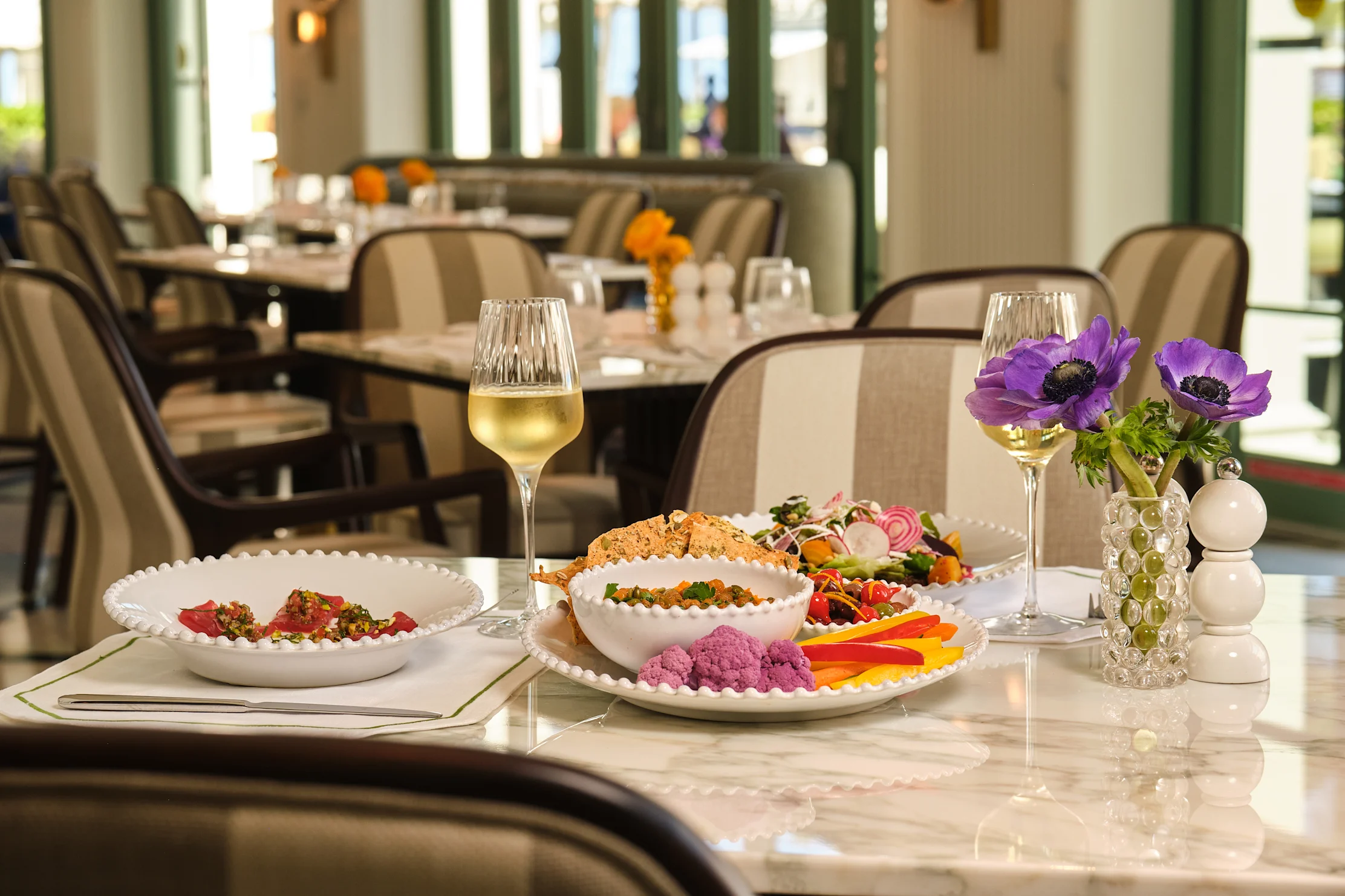 Elegant restaurant table with colorful appetizer plates, white wine and purple flower centerpiece.