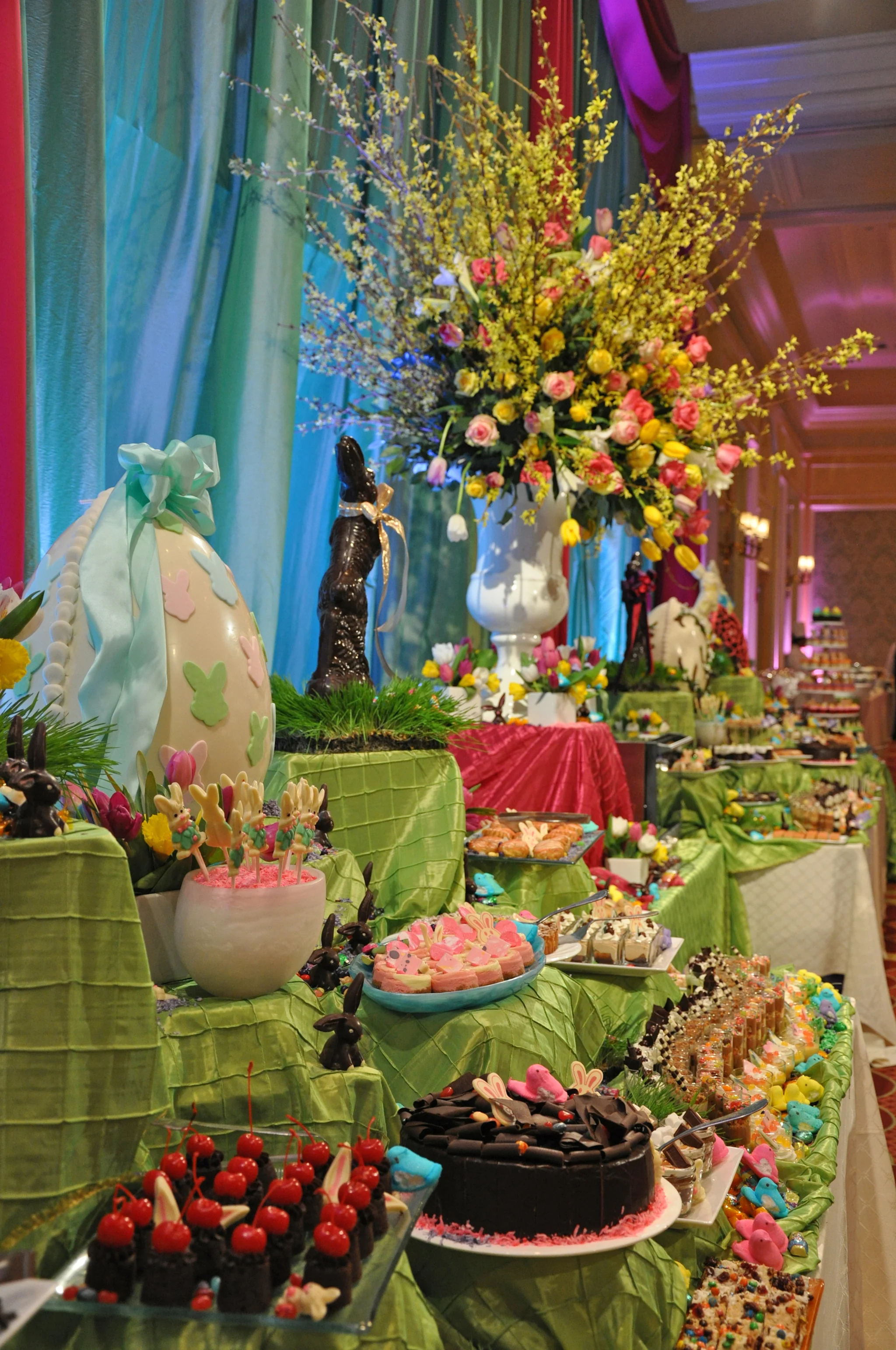 Easter dessert buffet with colorful treats, decorated egg, chocolate bunny, and spring flower arrangement.
