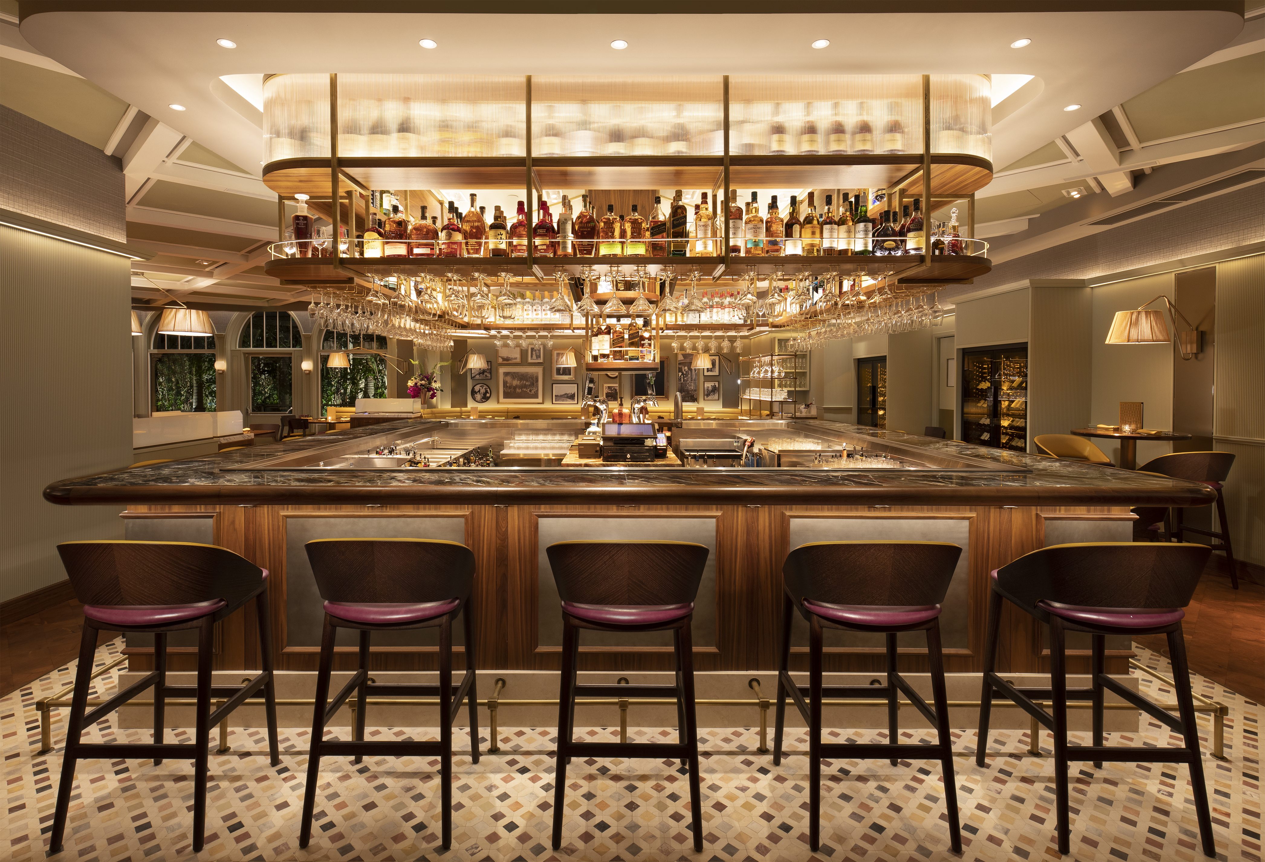 Upscale hotel bar with wooden counter, burgundy leather stools, and illuminated liquor display.