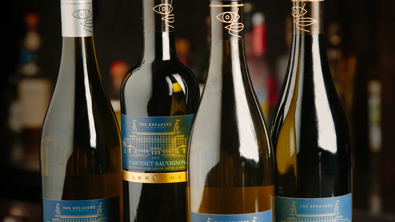 Four wine bottles with blue and gold labels displayed on a reflective bar surface with blurred bottles in the background.