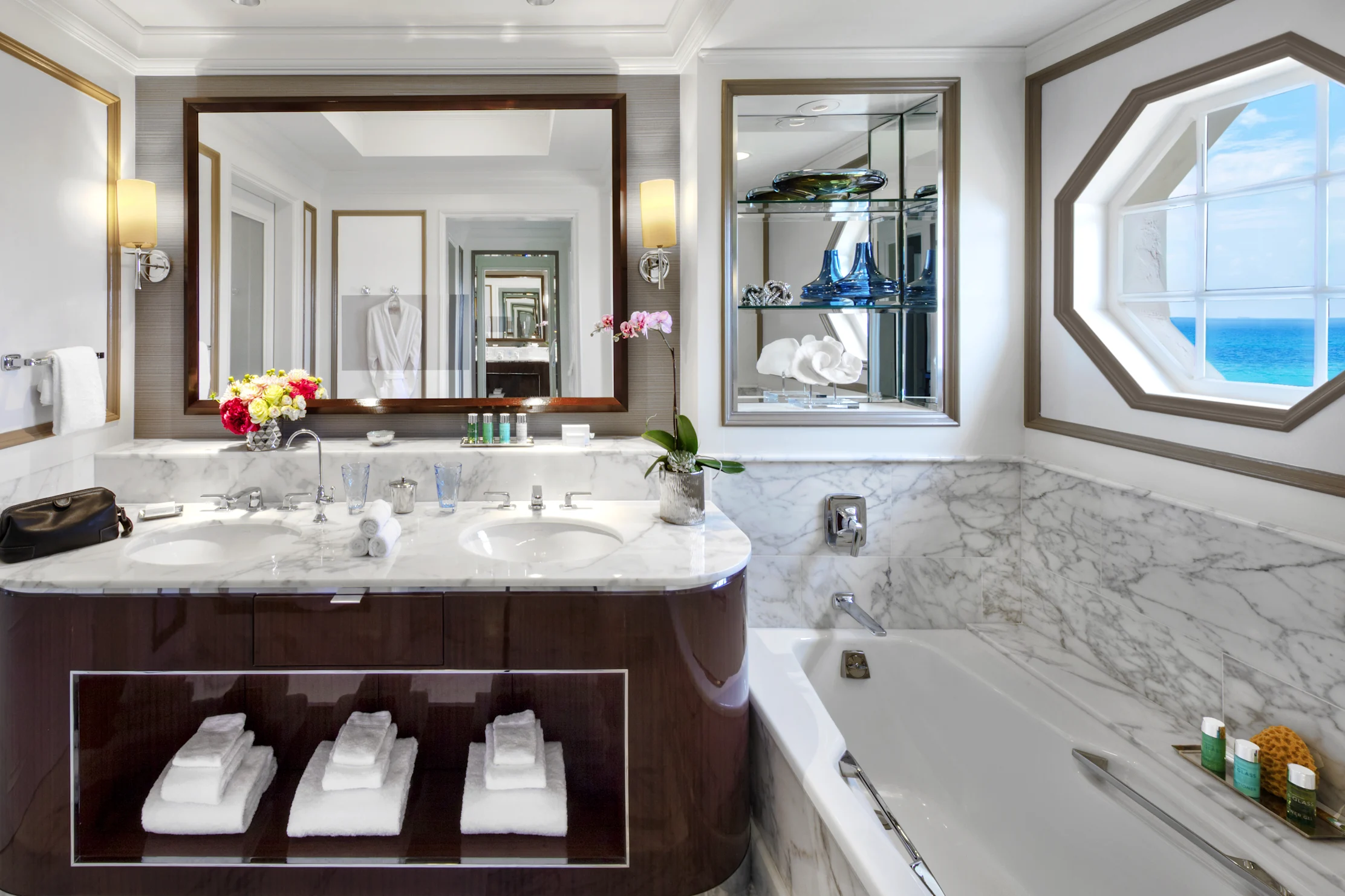 Luxury bathroom with white marble countertops, dark wood vanity, large mirror, and ocean view window.