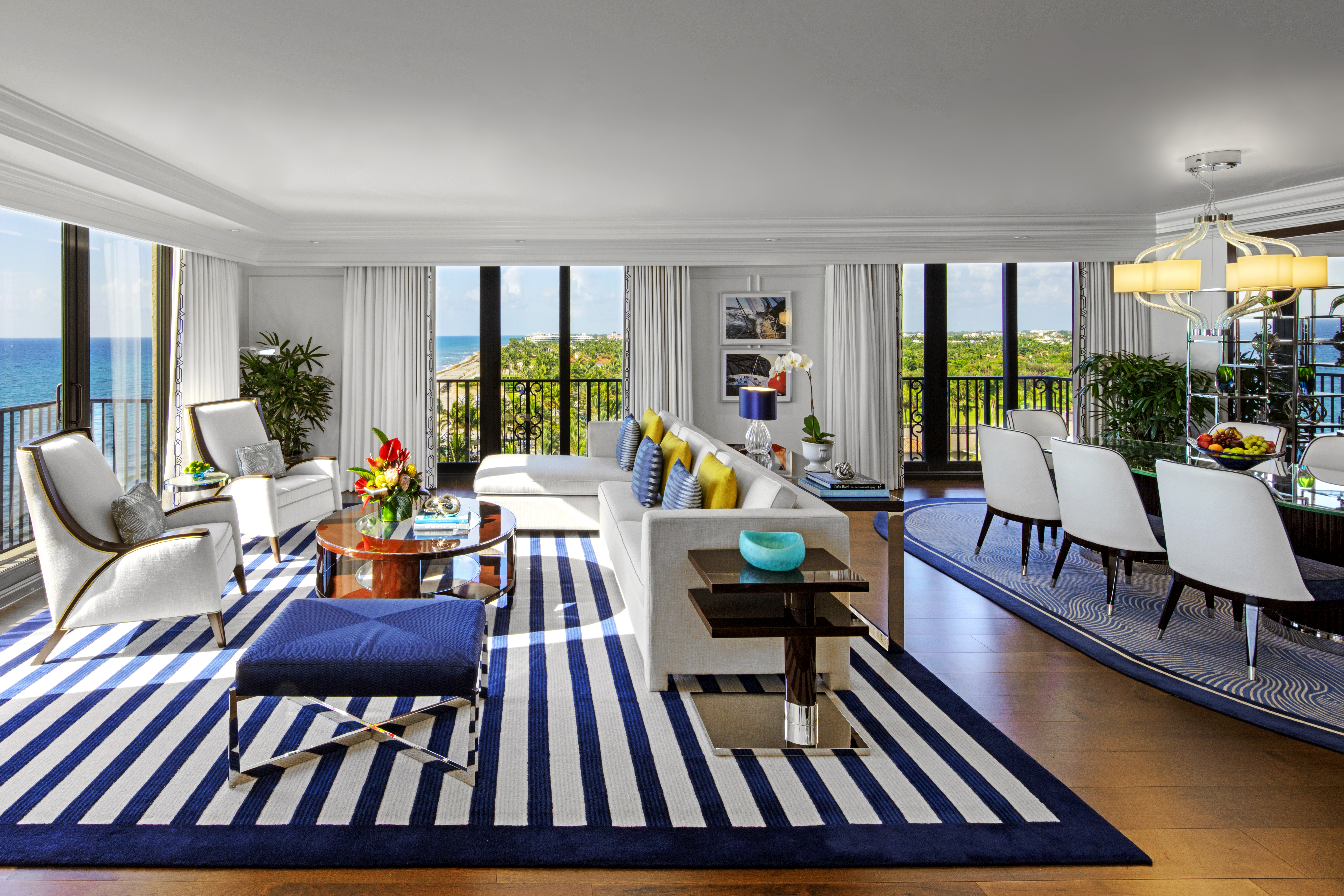 Bright modern living room with blue and white striped rug, white furniture, and ocean view balcony.
