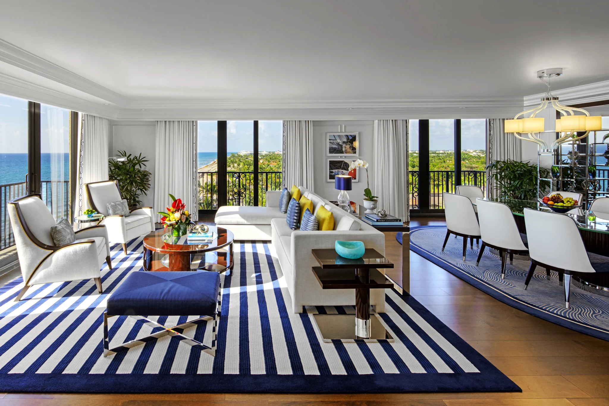 Bright modern living room with blue and white striped rug, white furniture, and ocean view balcony.