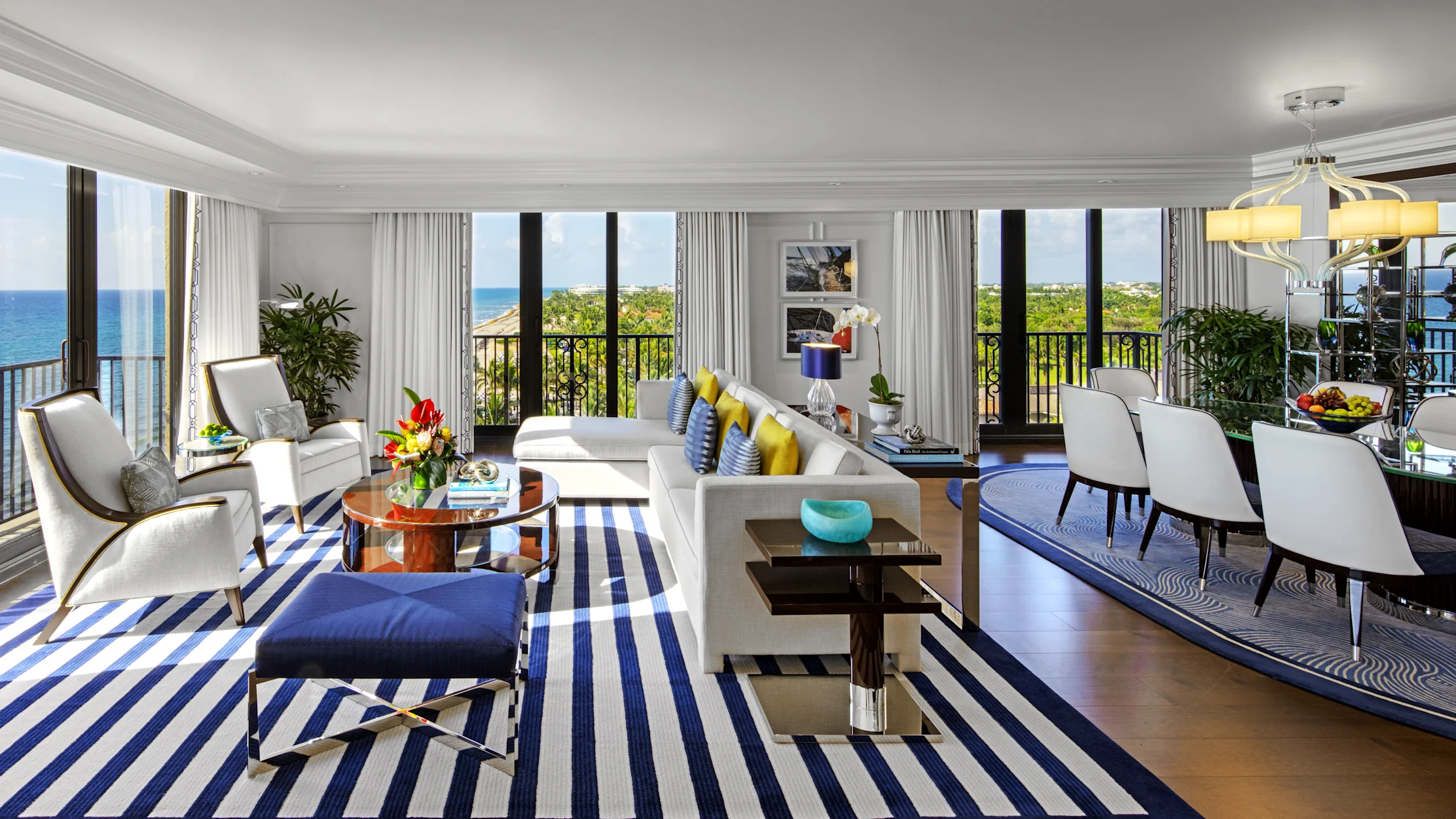 Bright modern living room with blue and white striped rug, white furniture, and ocean view balcony.