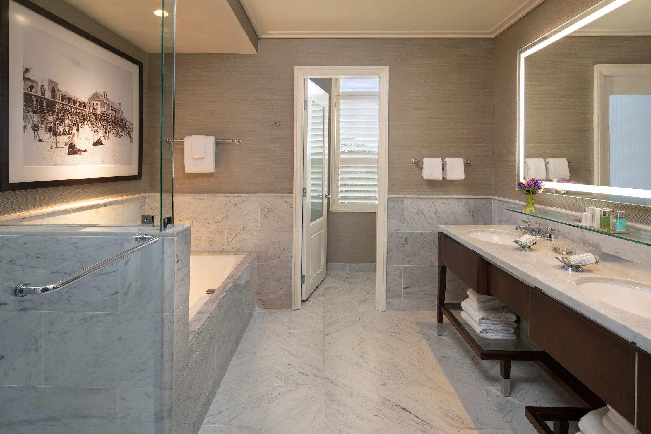 Luxury bathroom with marble tub, glass shower, double vanity, and backlit mirror in neutral tones.