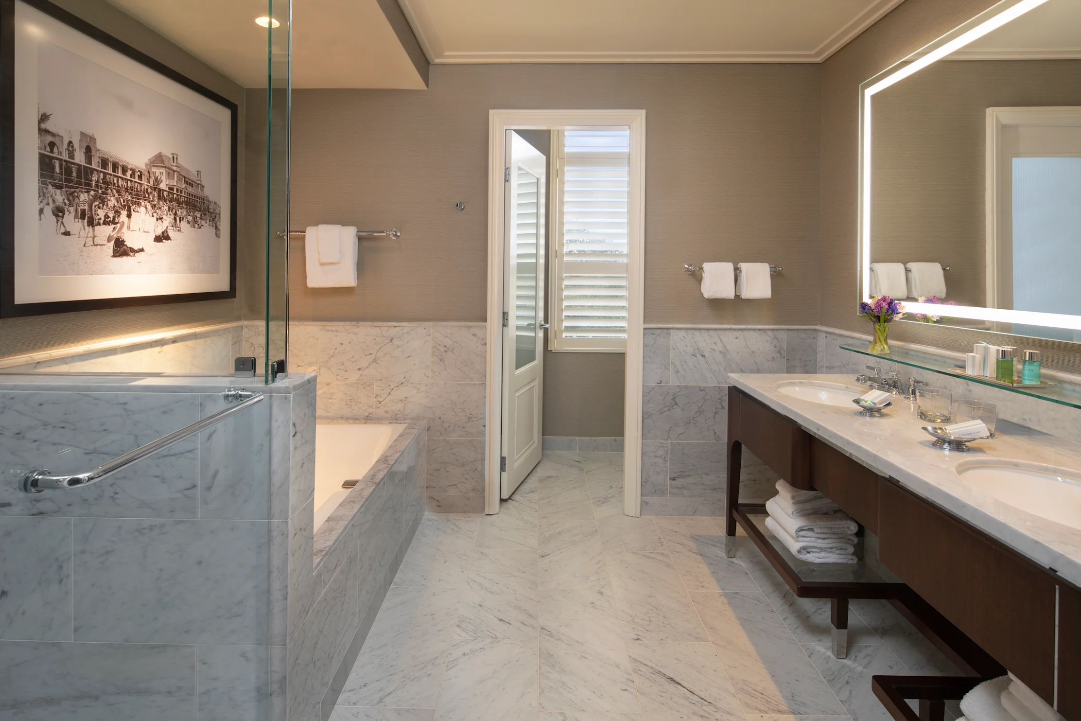 Luxury bathroom with marble tub, glass shower, double vanity, and backlit mirror in neutral tones.