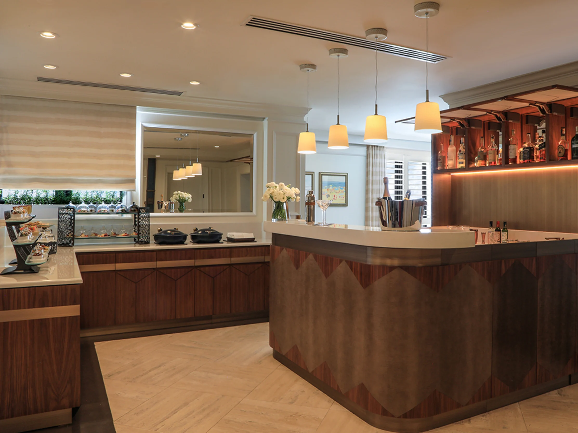 Modern hotel breakfast area with wooden buffet counter, pendant lights, and bar with illuminated shelving.