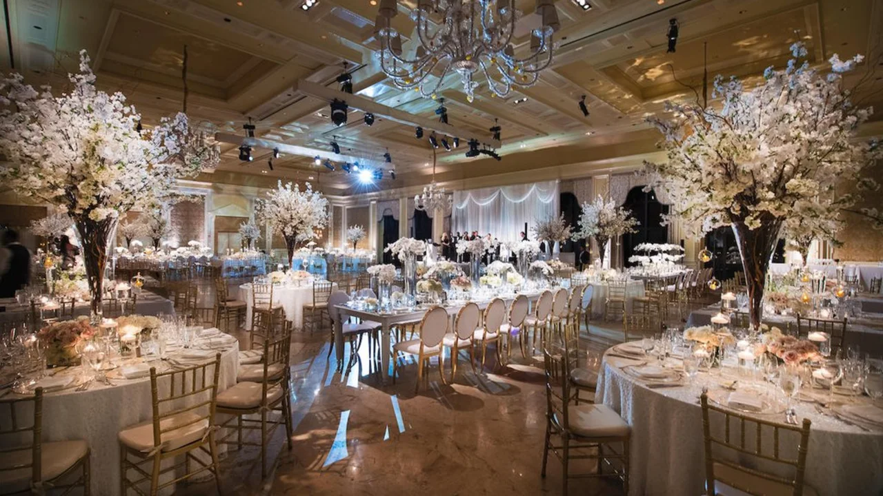Elegant wedding reception ballroom with white floral centerpieces, crystal chandeliers, and gold chairs