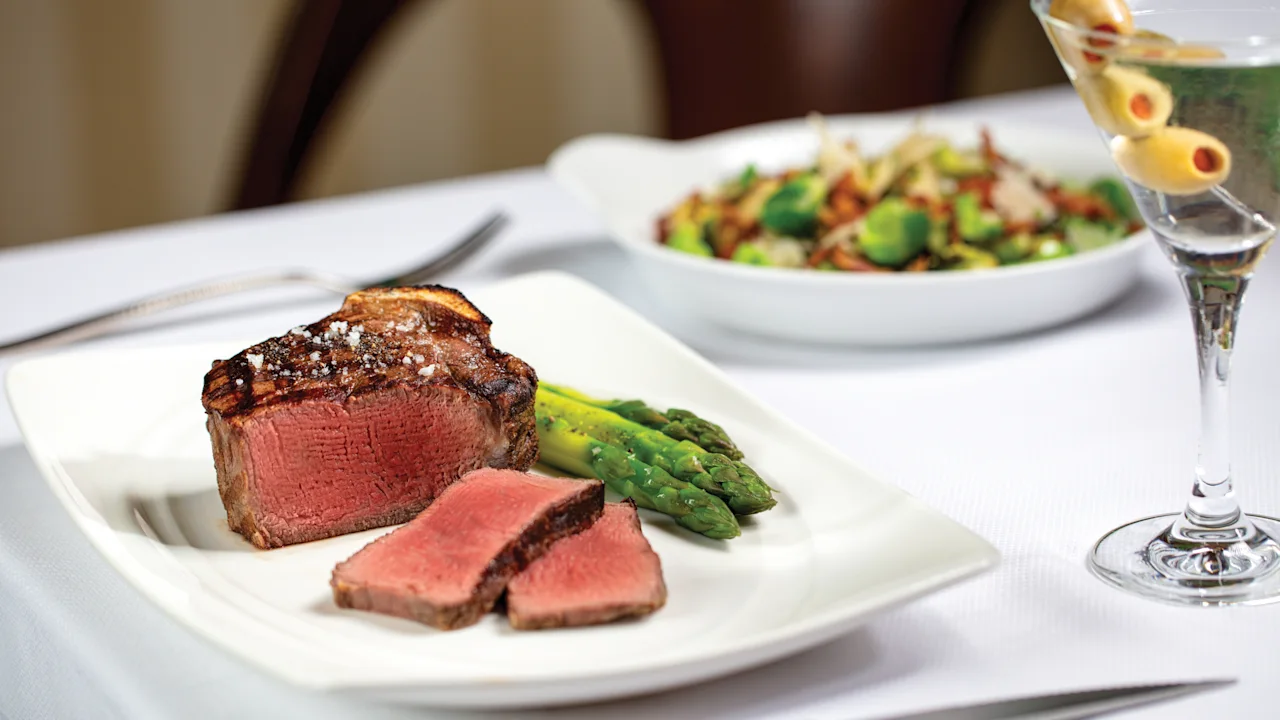 Grilled steak with asparagus on white plate, salad and martini with olives in background.