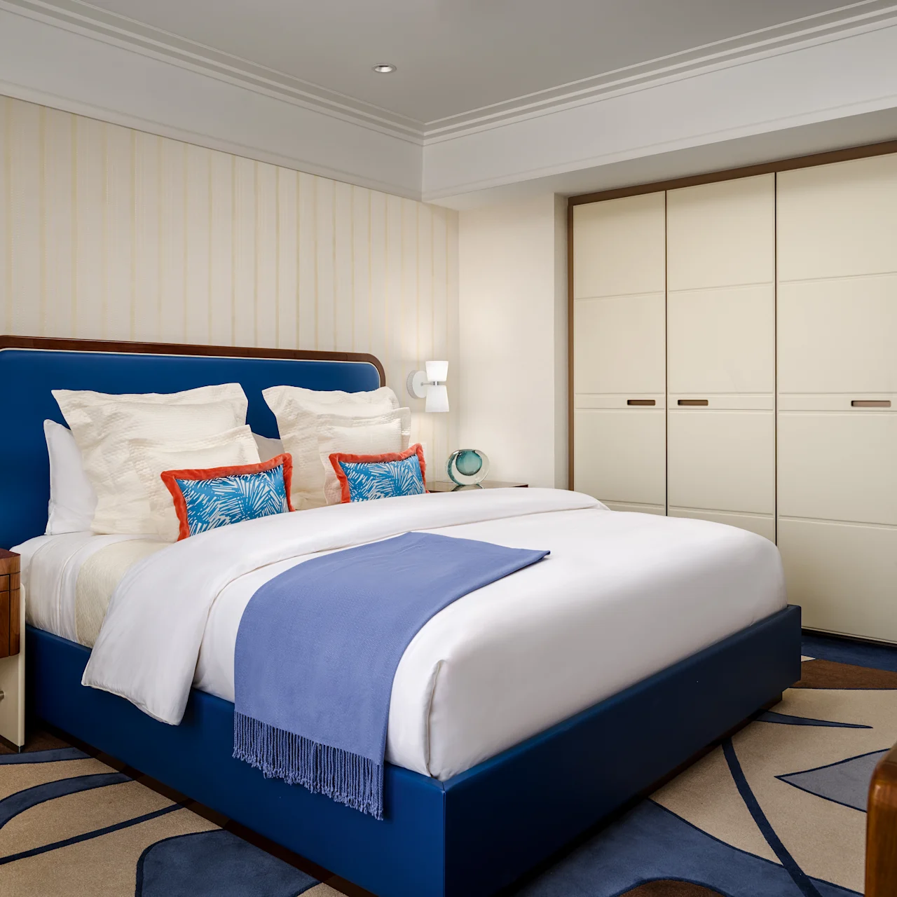 Modern bedroom with blue upholstered bed, white linens, cream wardrobes, and wood accents.