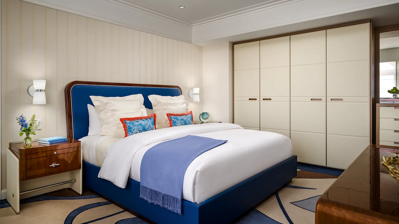Modern bedroom with blue upholstered bed, white linens, cream wardrobes, and wood accents.