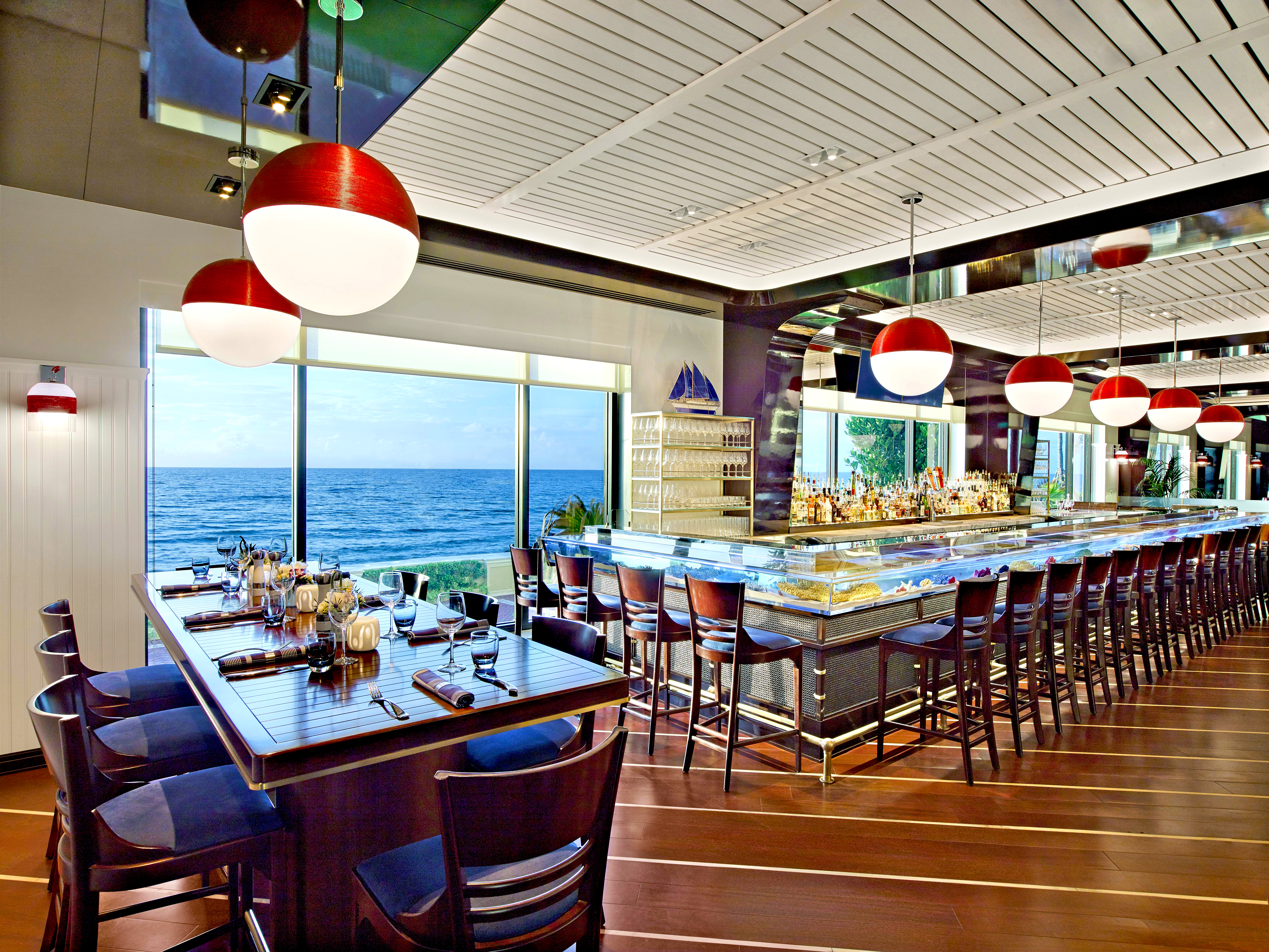 Modern oceanfront restaurant with red and white pendant lights, sushi bar, and ocean view windows.