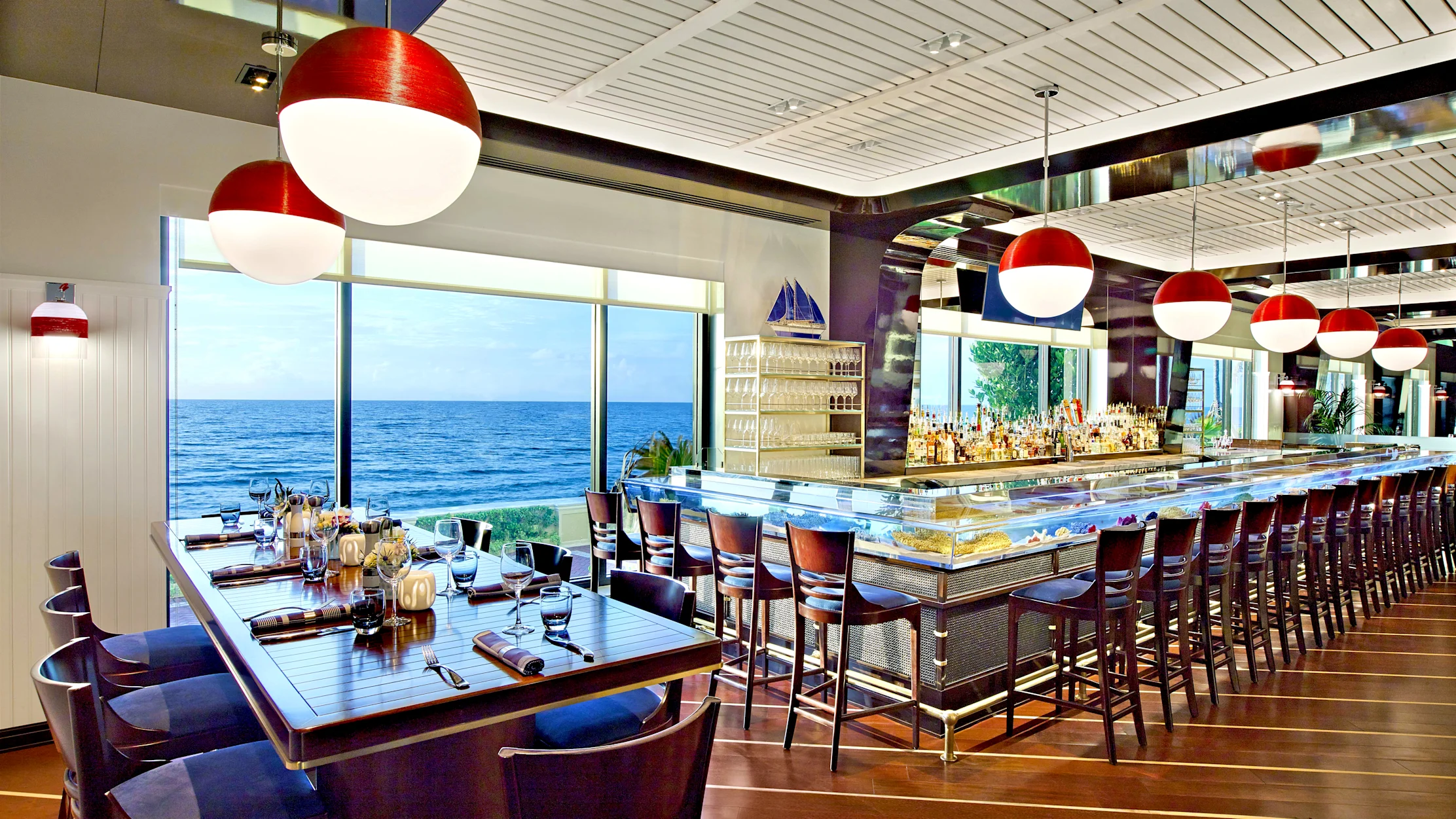Modern oceanfront restaurant with red and white pendant lights, sushi bar, and ocean view windows.