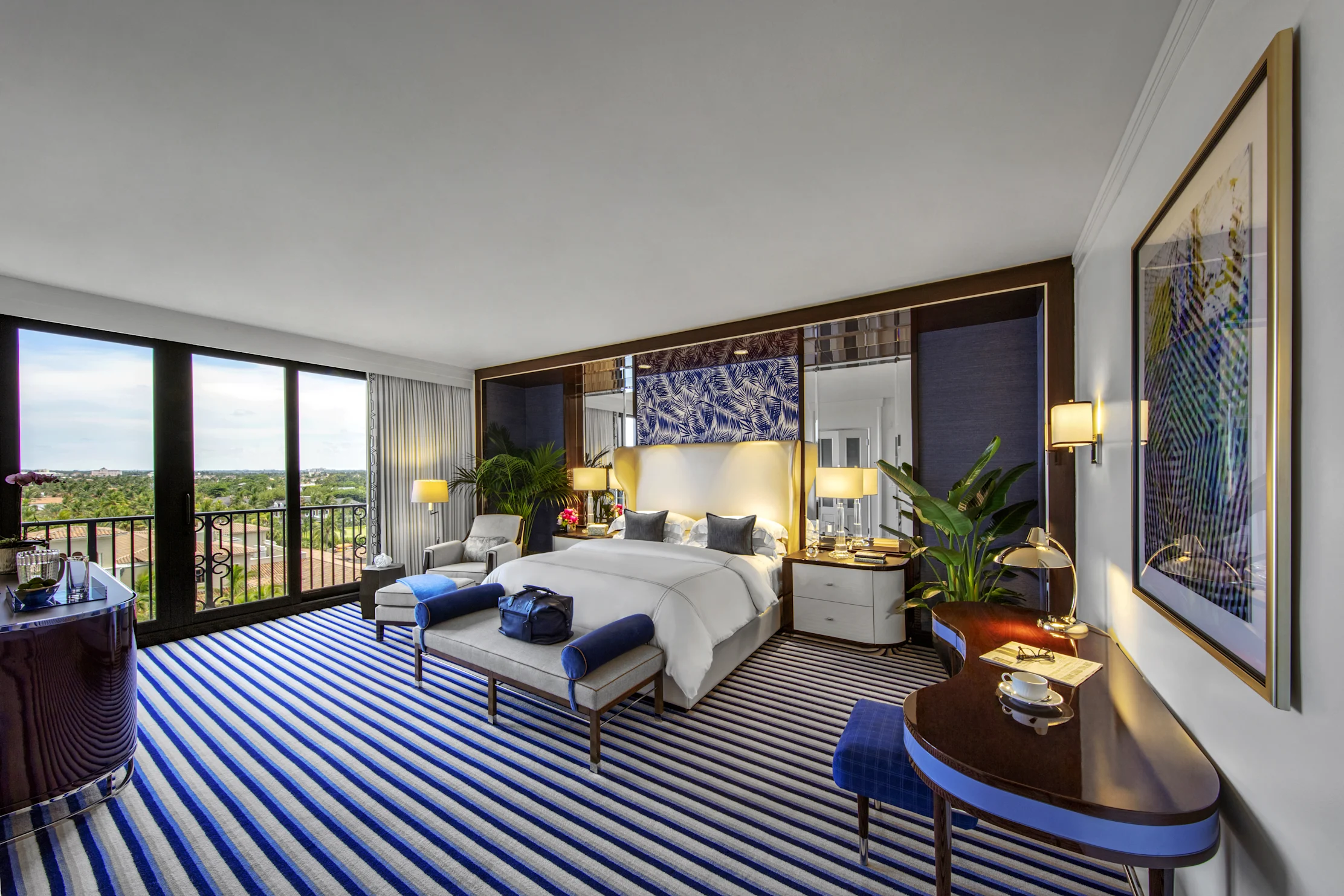 Luxury hotel bedroom with blue striped carpet, white bed, balcony view, and modern decor.