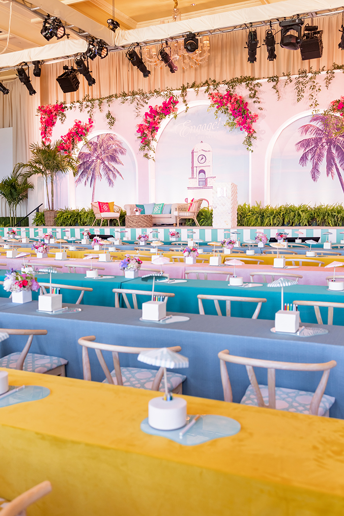 Colorful event venue with tropical theme, featuring pink floral arches, palm trees, and pastel tables.