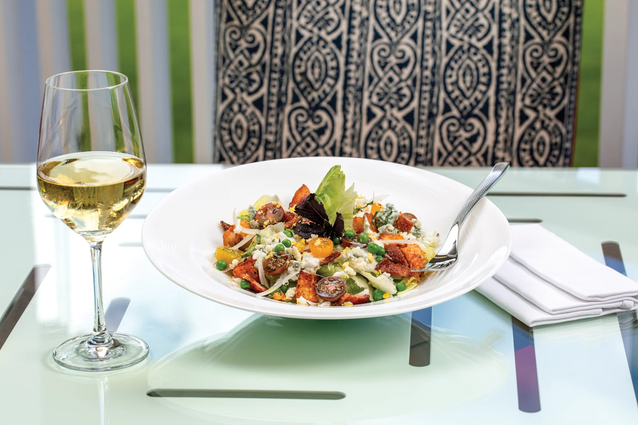 Colorful salad with vegetables and cheese on white plate beside glass of white wine on table.