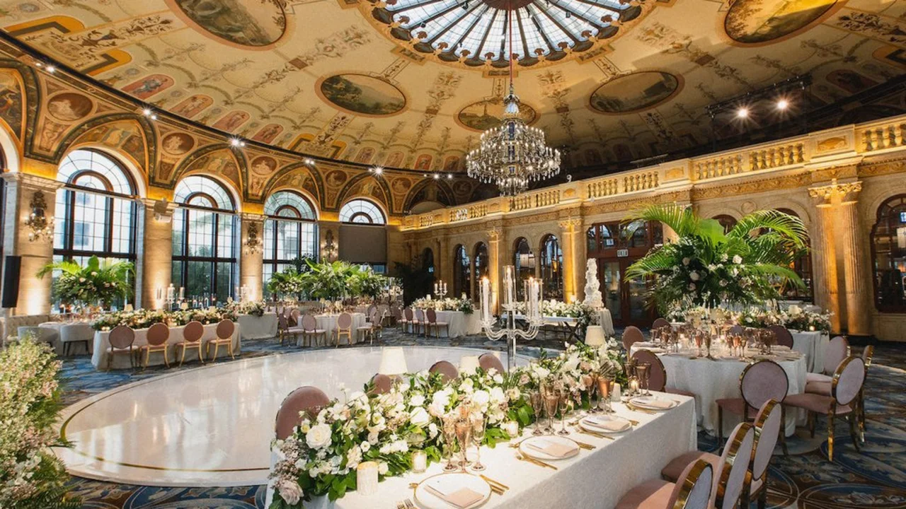 Elegant ballroom with ornate painted ceiling, crystal chandelier, and formal dining tables with floral centerpieces.
