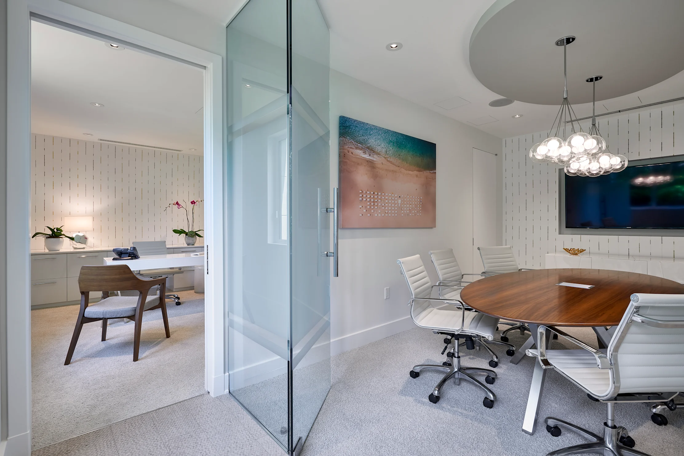 Modern office with glass door, wooden conference table, white chairs, and coastal artwork.