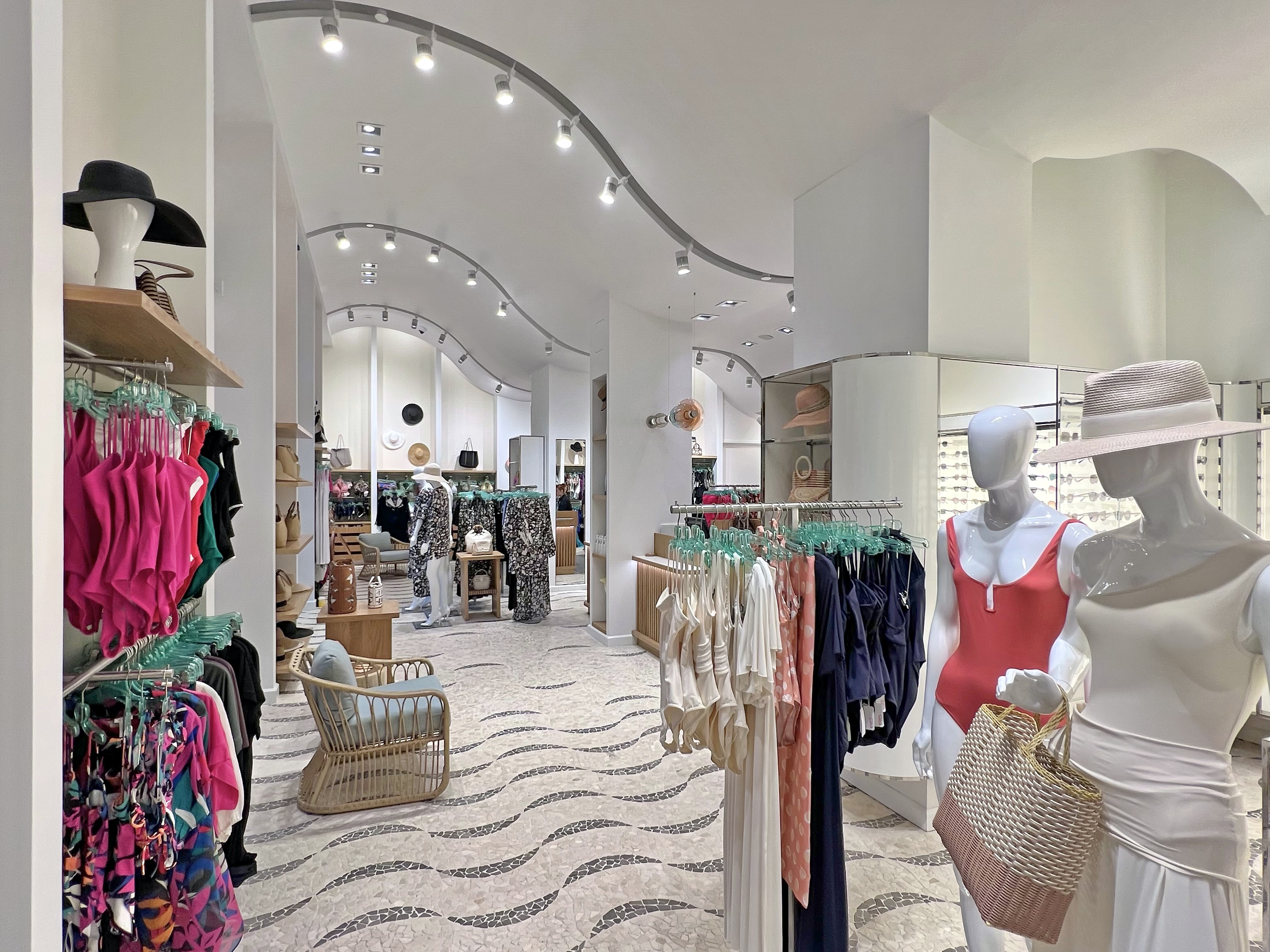 Modern clothing boutique interior with curved track lighting, white walls, and colorful apparel displays.