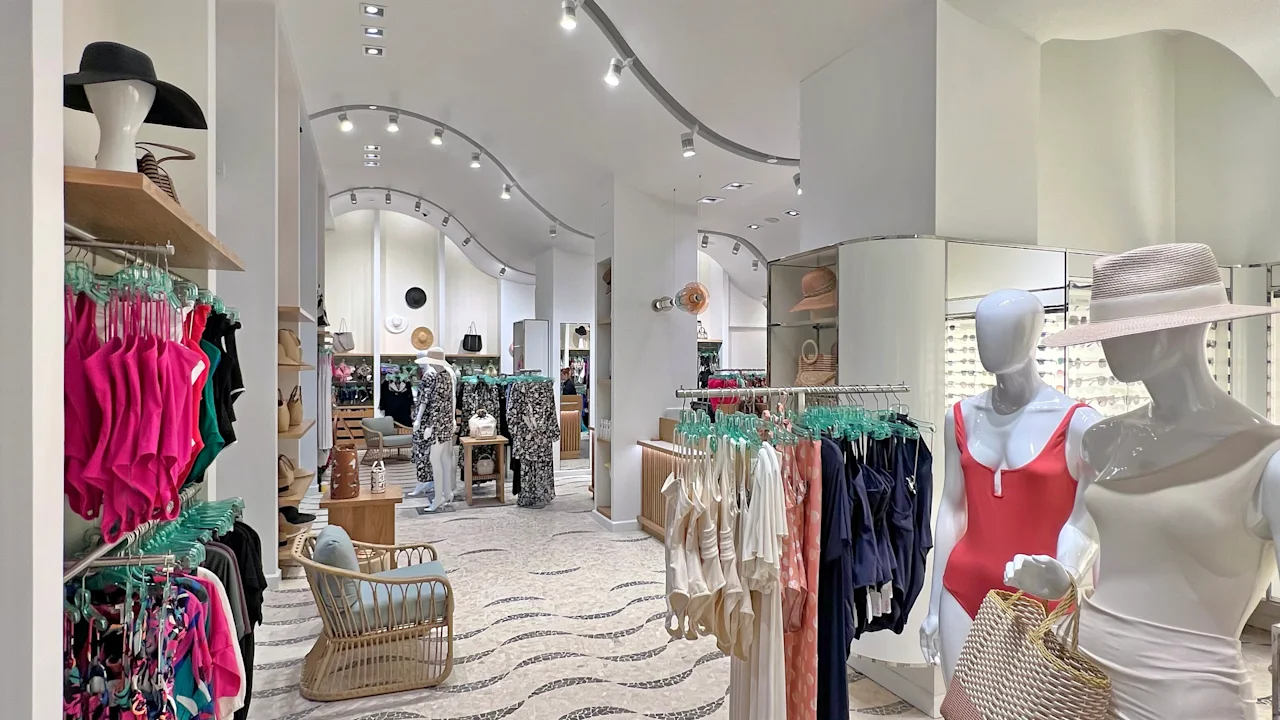 Modern clothing boutique interior with curved track lighting, white walls, and colorful apparel displays.
