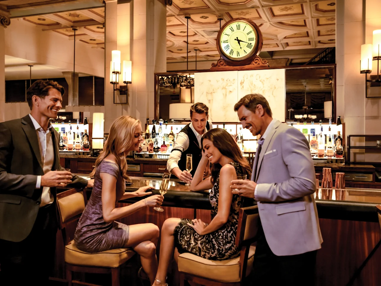 Elegantly dressed guests enjoying cocktails at an upscale hotel bar with ornate ceiling and large clock.