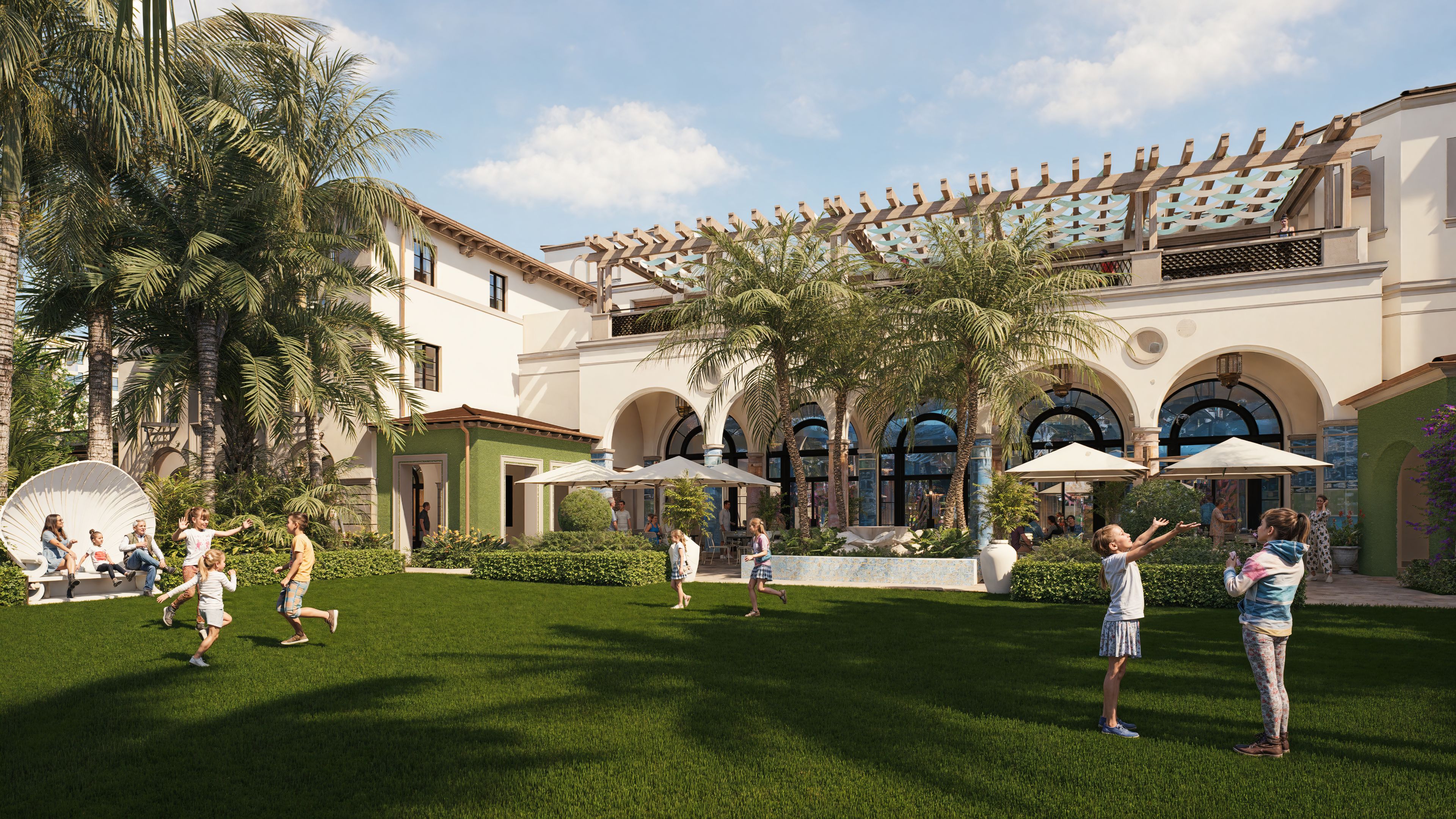 Children playing on green lawn in front of white Mediterranean-style resort with palm trees and arches.