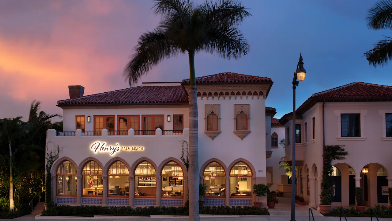 Mediterranean-style building with arched windows and red tile roof at dusk with palm tree.