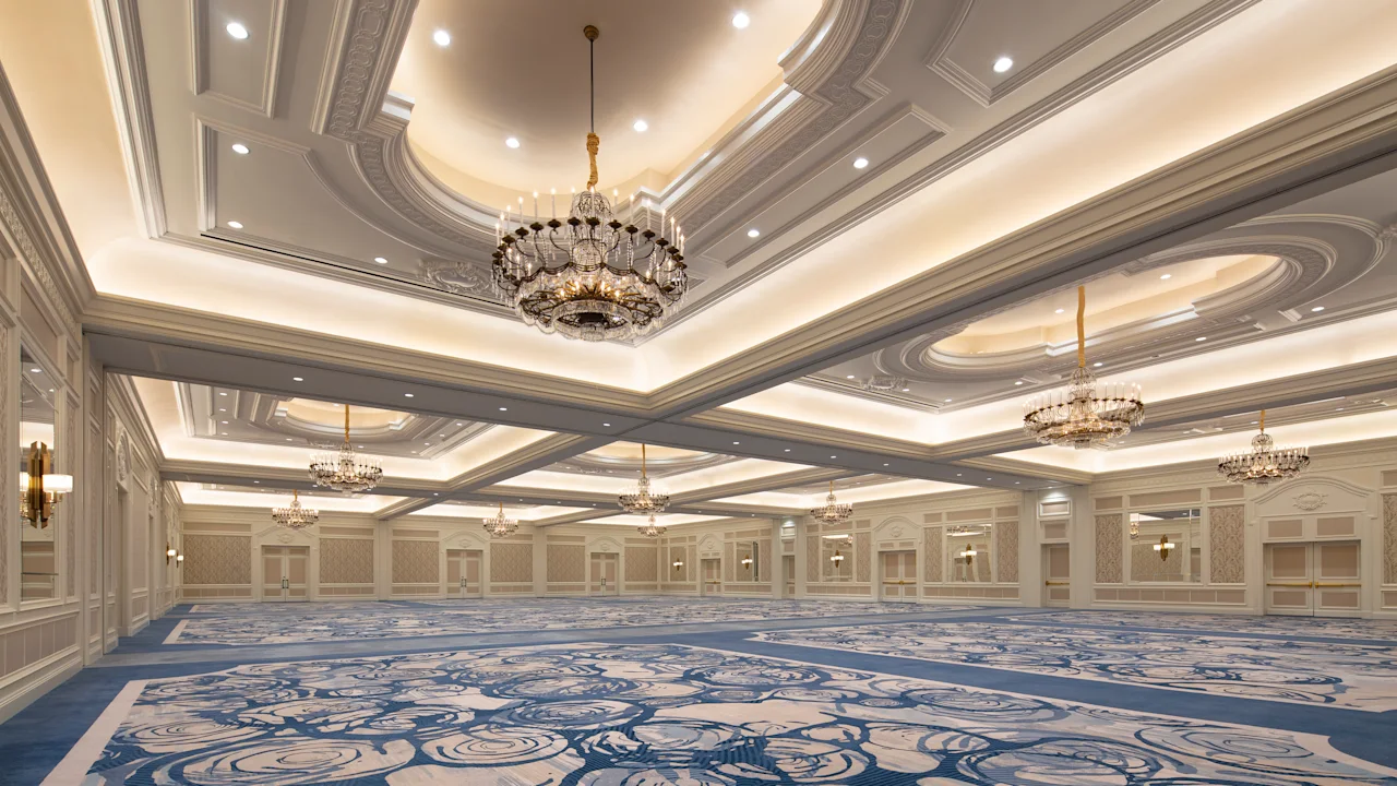 Elegant ballroom with ornate ceiling, crystal chandeliers, and blue patterned carpet in neutral tones.