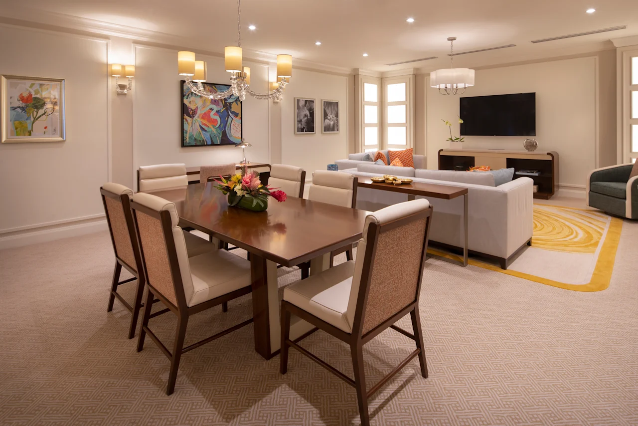 Modern hotel suite with dining table, living area, colorful artwork, and yellow accent rug.