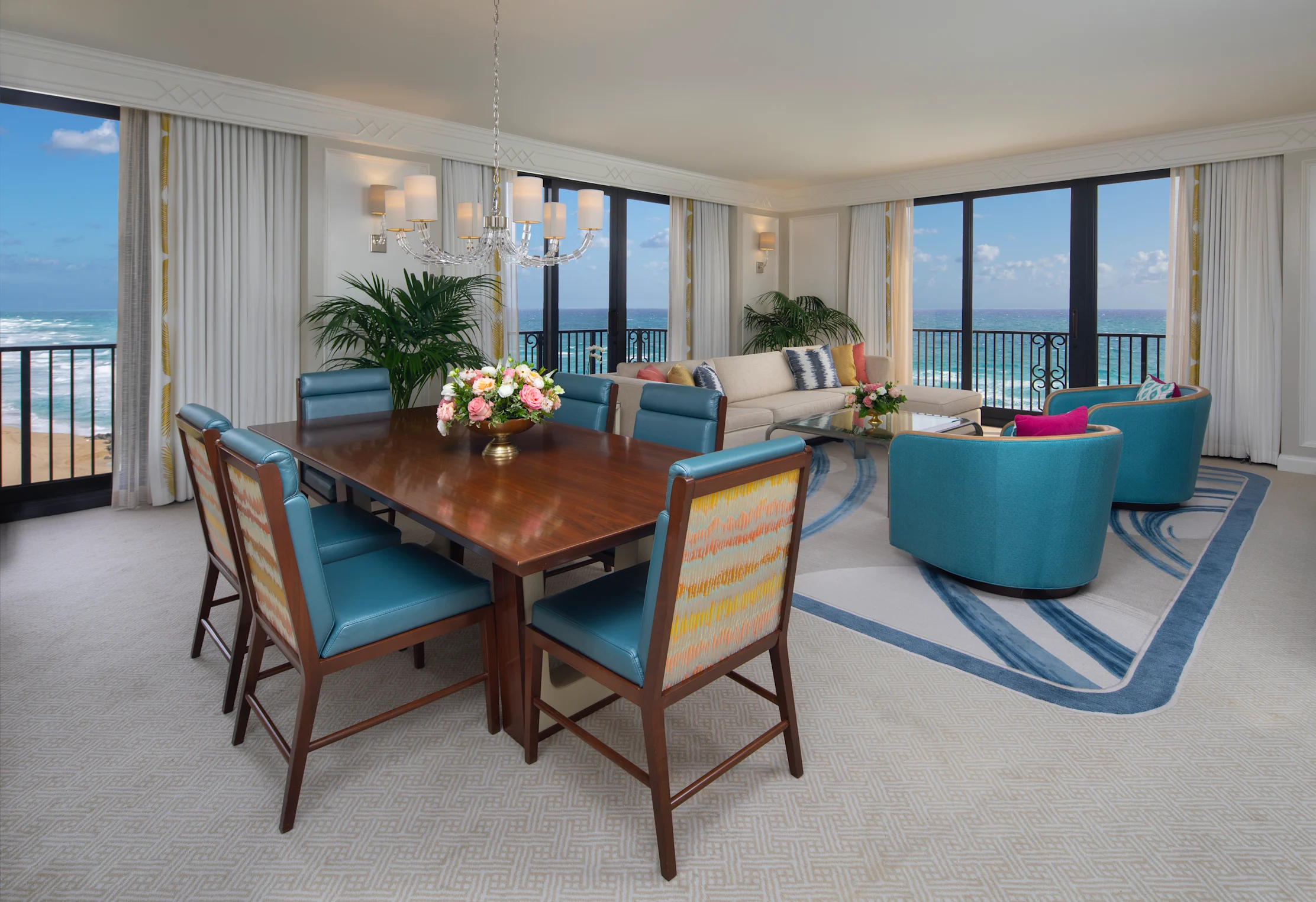 Luxury oceanfront suite with dining table, teal chairs, living area, and panoramic beach views.