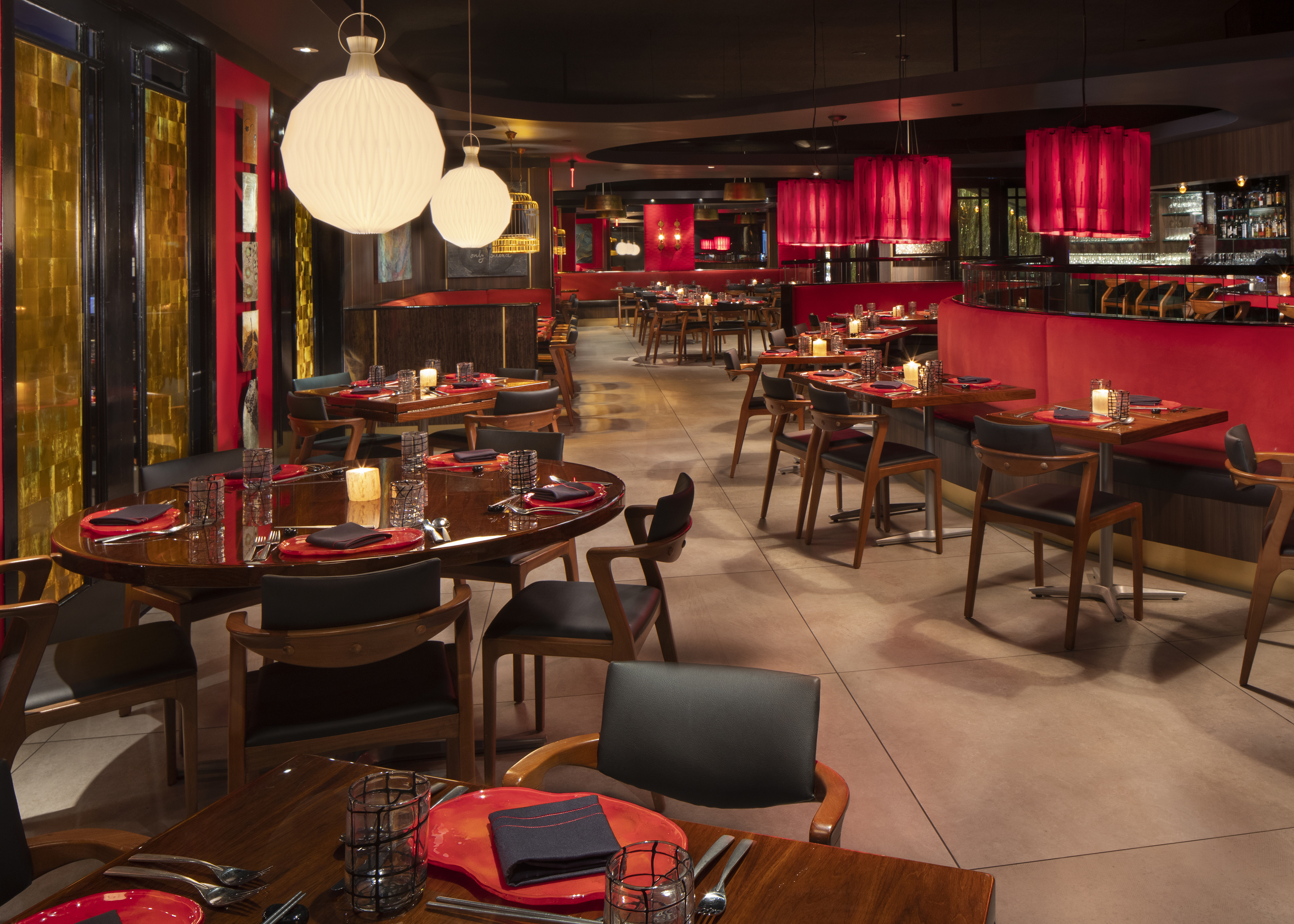 Modern restaurant interior with red accents, wooden tables, black chairs, and white globe pendant lights.