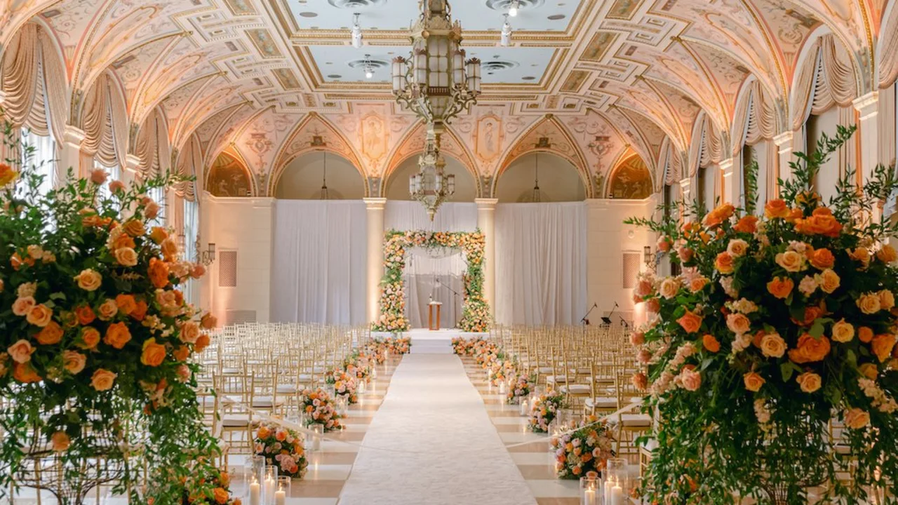 Elegant wedding ceremony venue with ornate ceiling, white aisle, gold chairs, and orange floral arrangements.