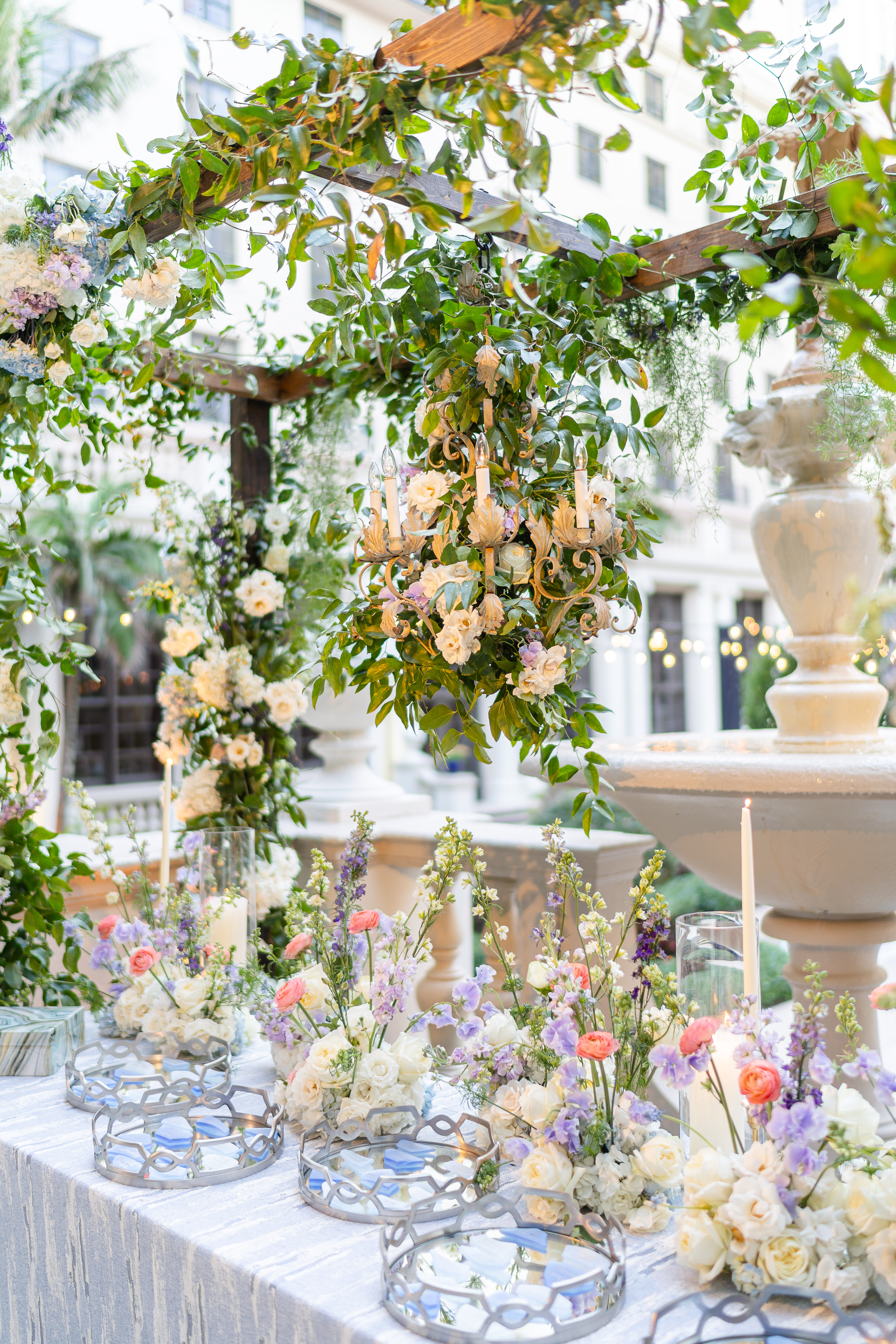Elegant outdoor wedding reception with lush greenery, chandelier, and pastel floral arrangements.