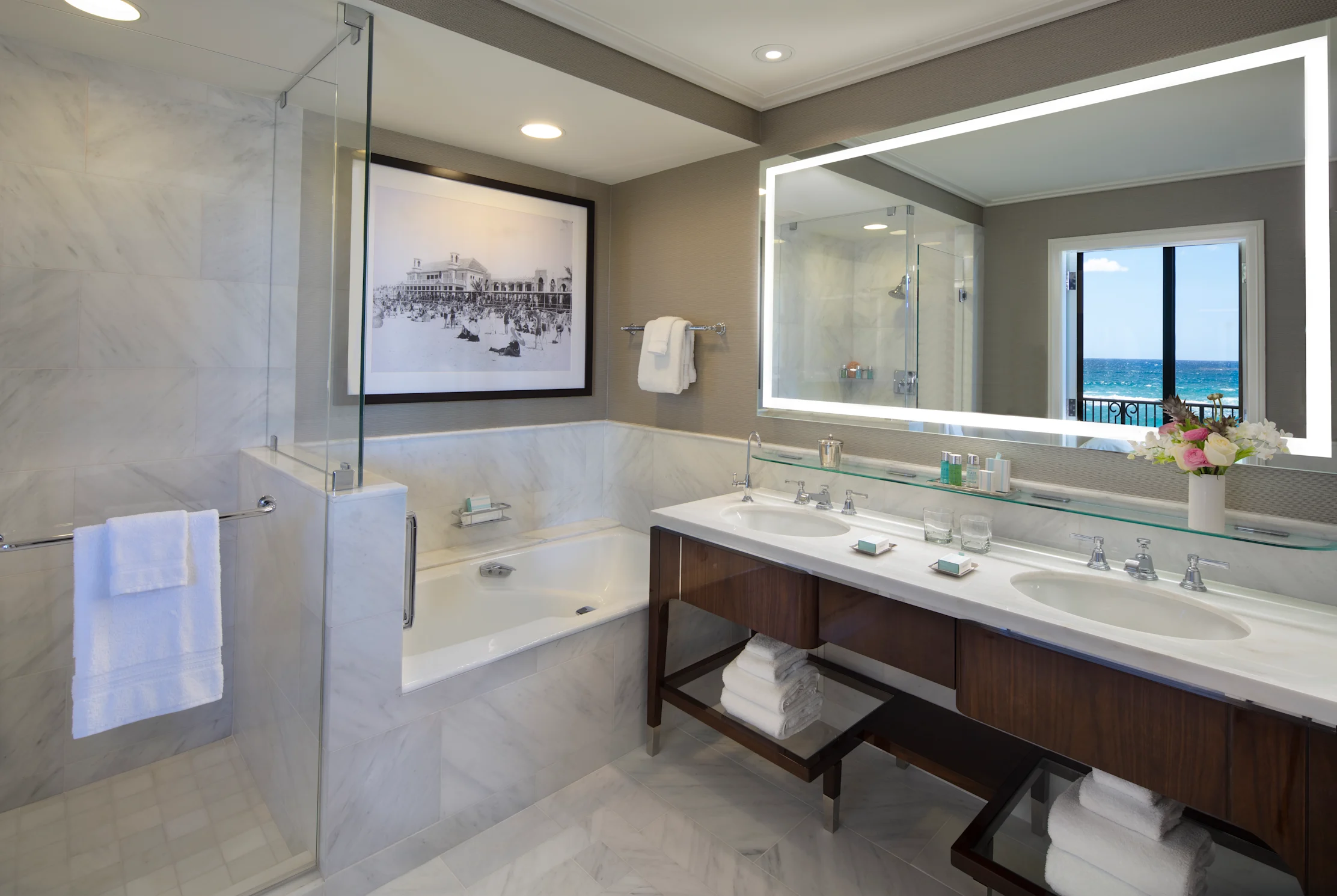 Luxury hotel bathroom with marble finishes, double vanity, soaking tub, and ocean view mirror.