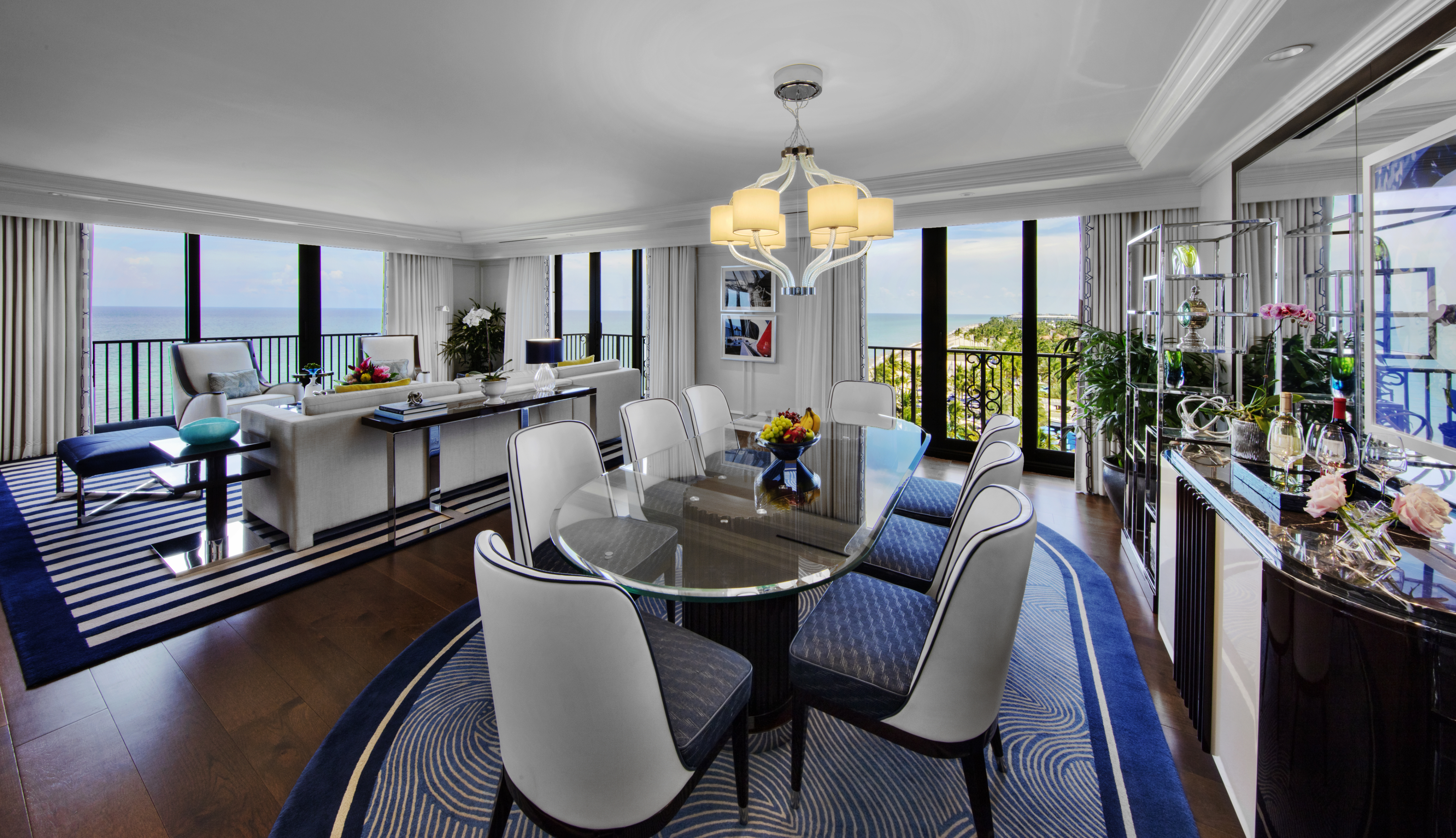 Luxury hotel suite with ocean view, featuring dining area and living room with blue and white decor.