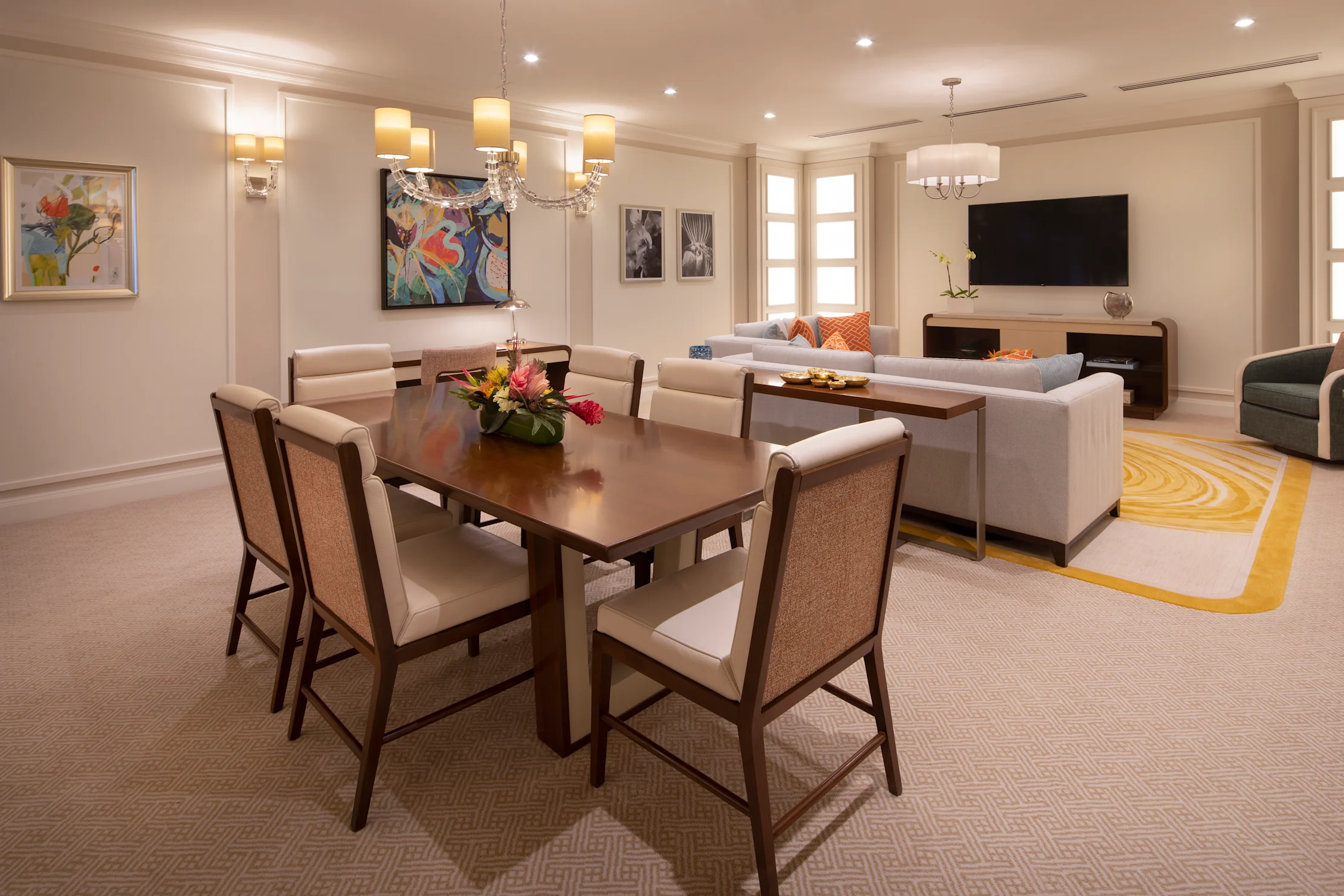 Modern hotel suite with dining table, living area, colorful artwork, and yellow accent rug.