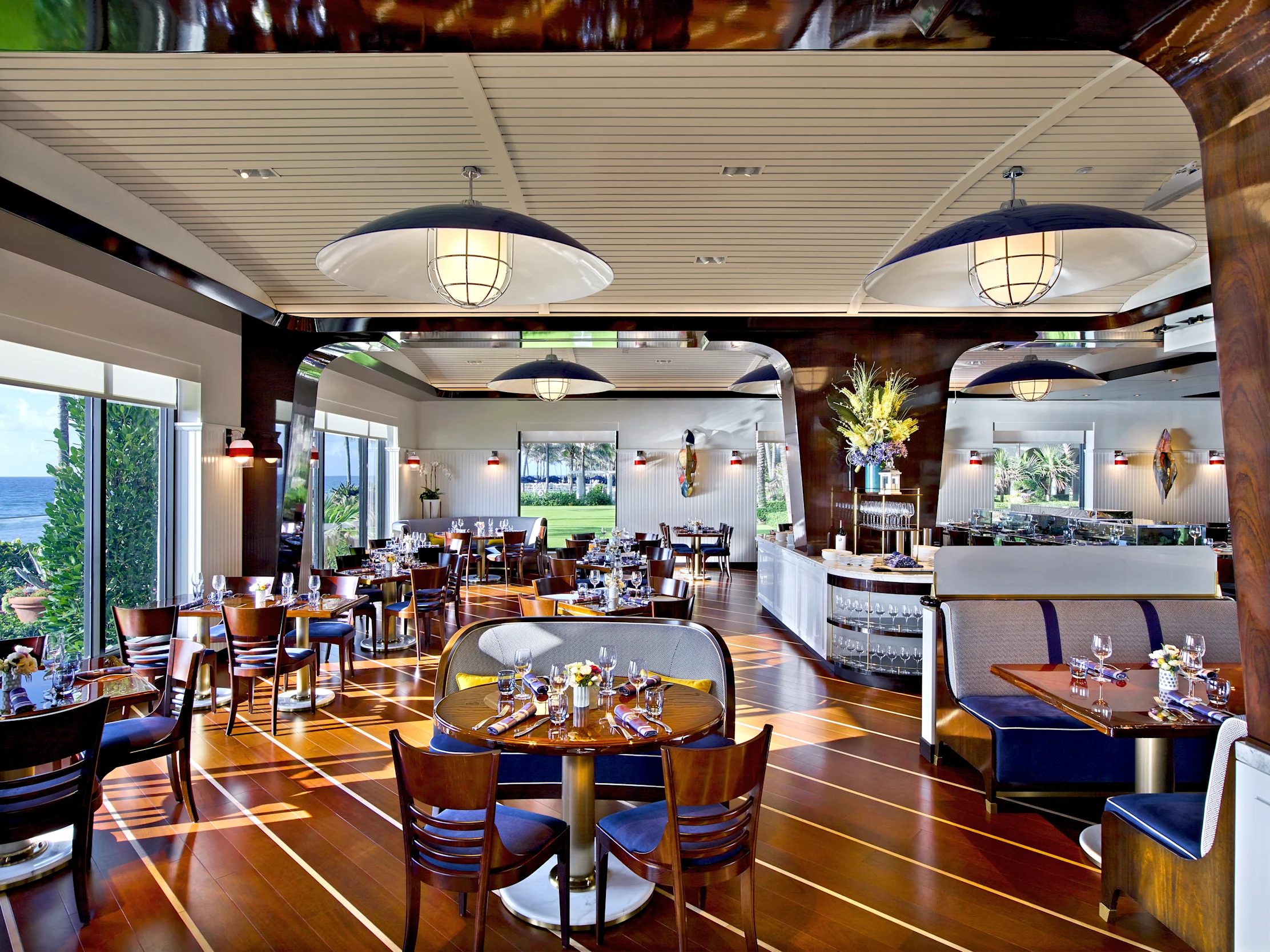 Upscale restaurant interior with wooden floors, nautical pendant lights, ocean views, and booth seating.