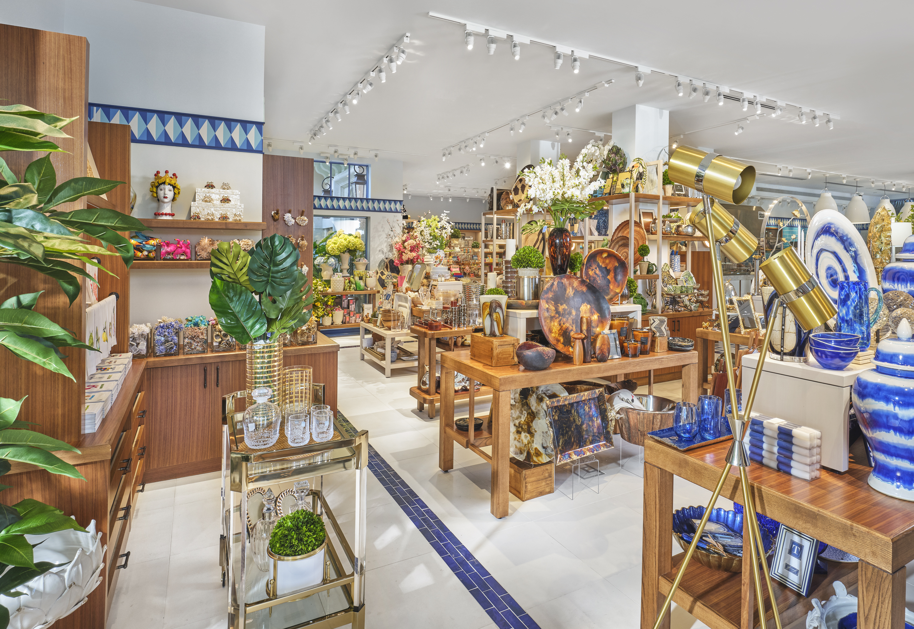 Bright retail store interior with wooden displays, colorful home decor items, plants, and track lighting.