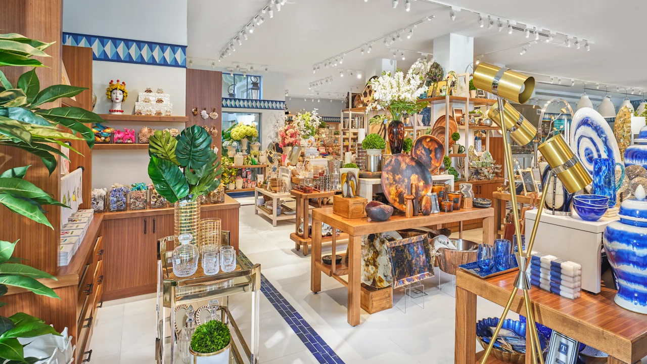 Bright retail store interior with wooden displays, colorful home decor items, plants, and track lighting.