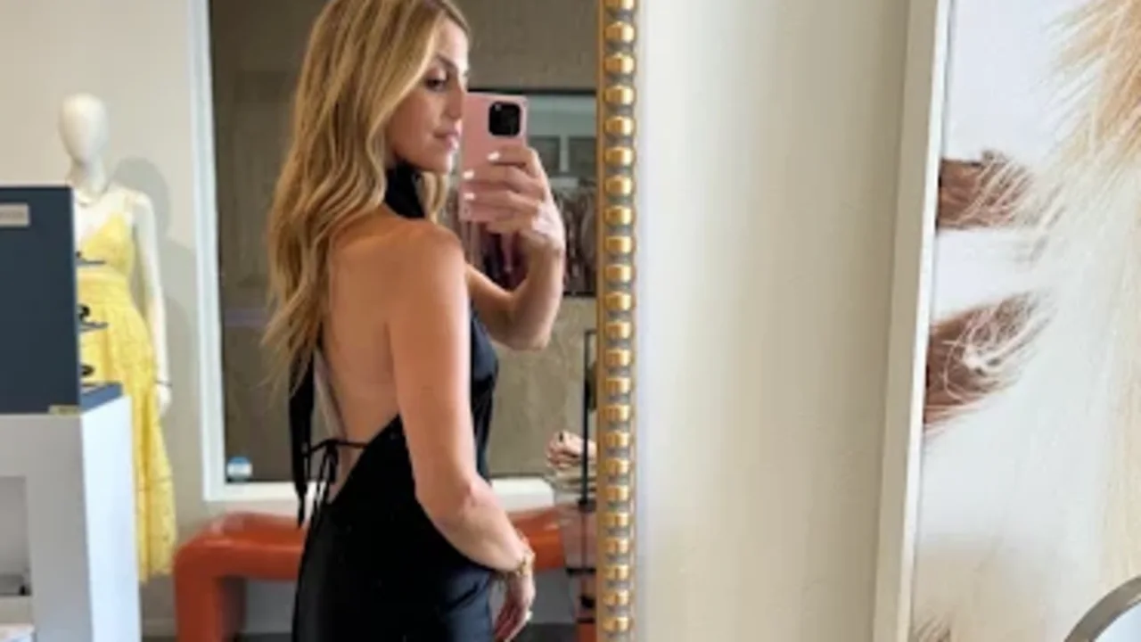 Woman in black halter dress taking mirror selfie with phone in modern interior with gold-framed mirror