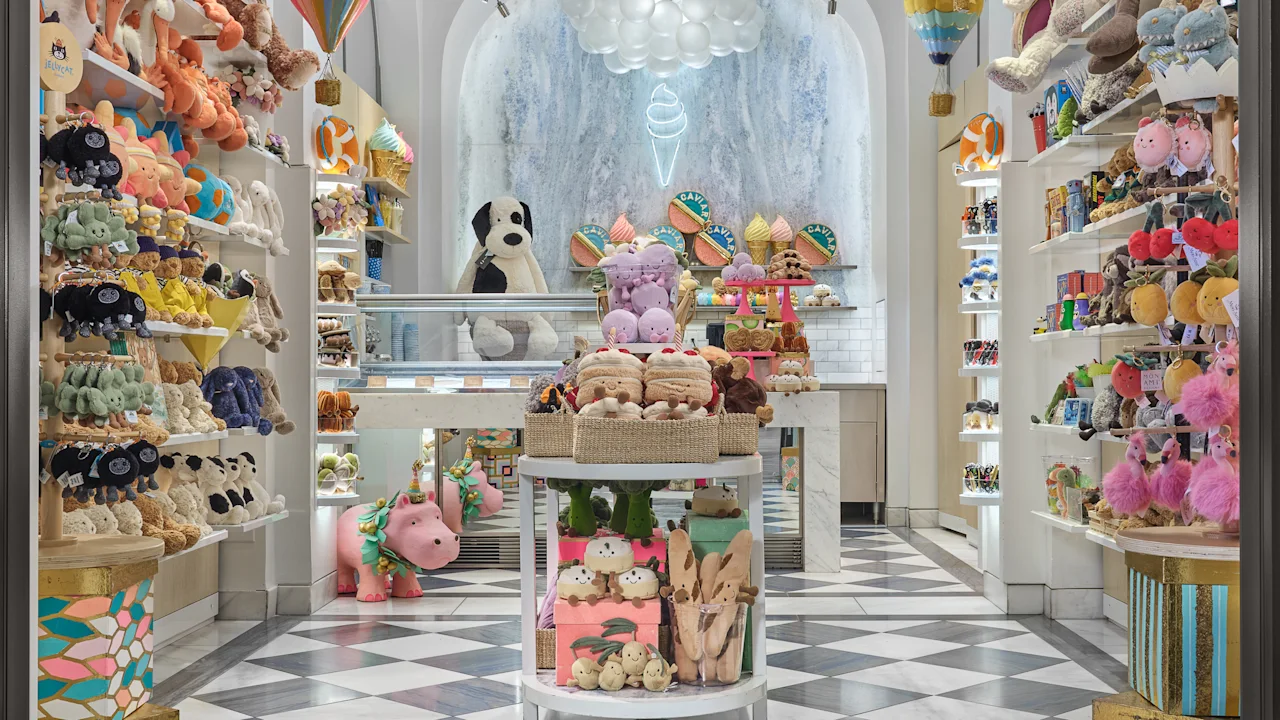 Whimsical toy store interior with white arched ceilings, cloud chandeliers, colorful plush toys on shelves, and checkered floor.