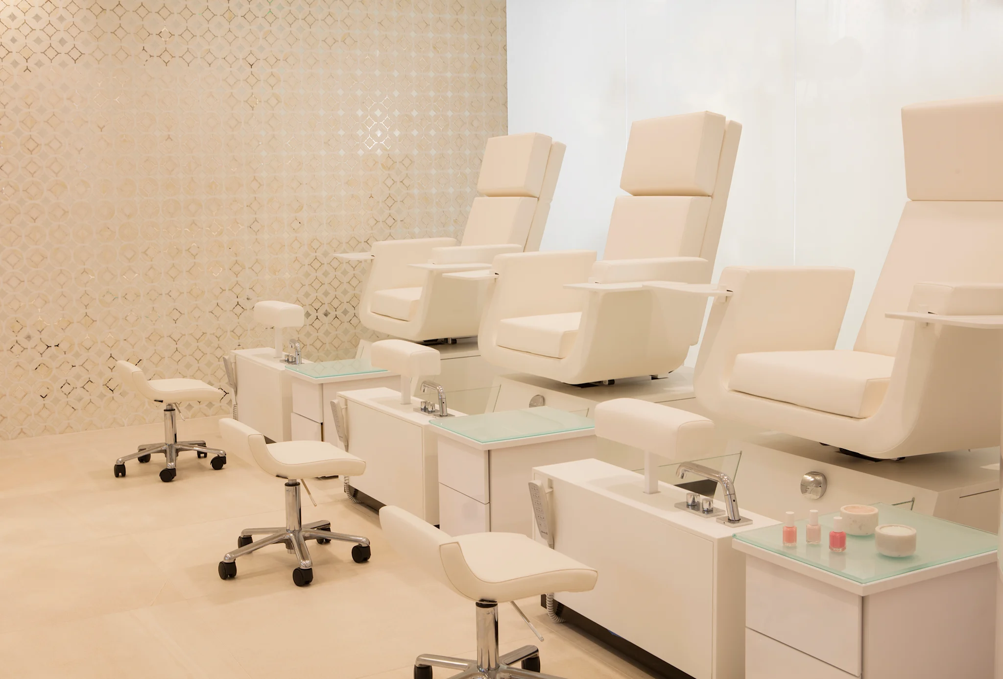 Modern white pedicure spa with reclining chairs, footbaths, and technician stools against decorative wall
