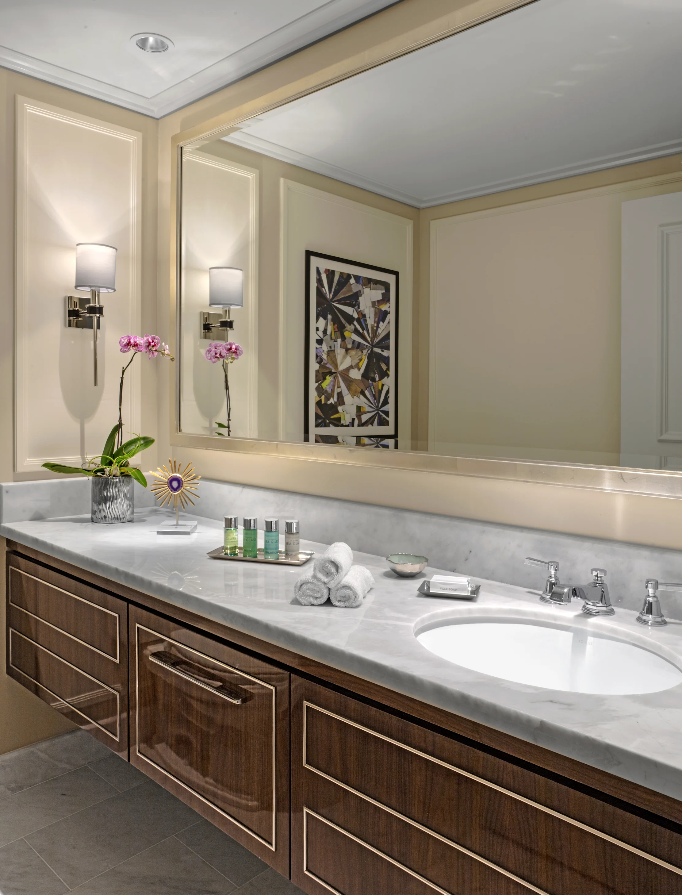 Elegant bathroom vanity with white marble countertop, dark wood cabinets, large mirror, and pink orchid.