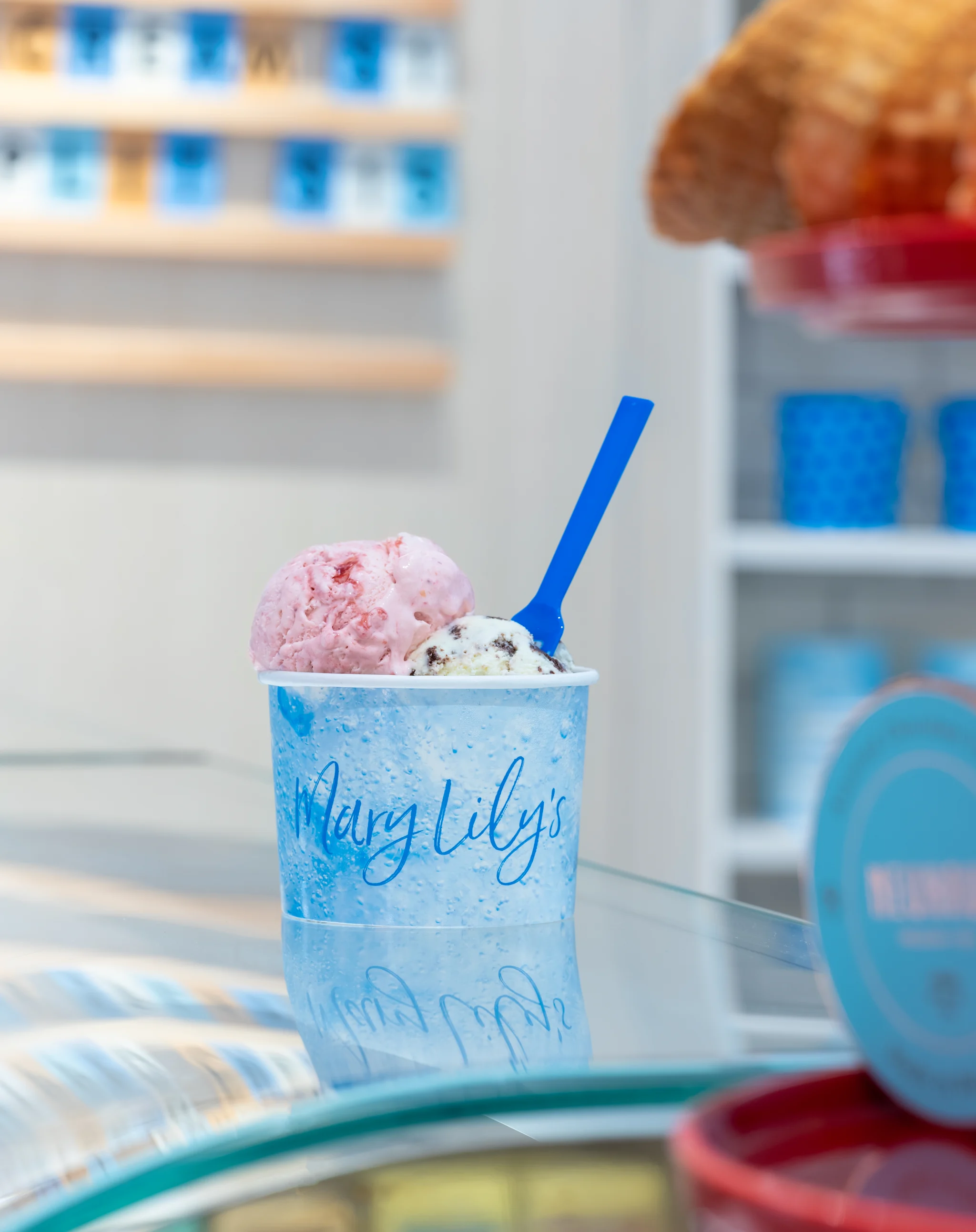 Ice cream scoops in a blue Mary Lily's cup with a blue spoon at an ice cream shop.