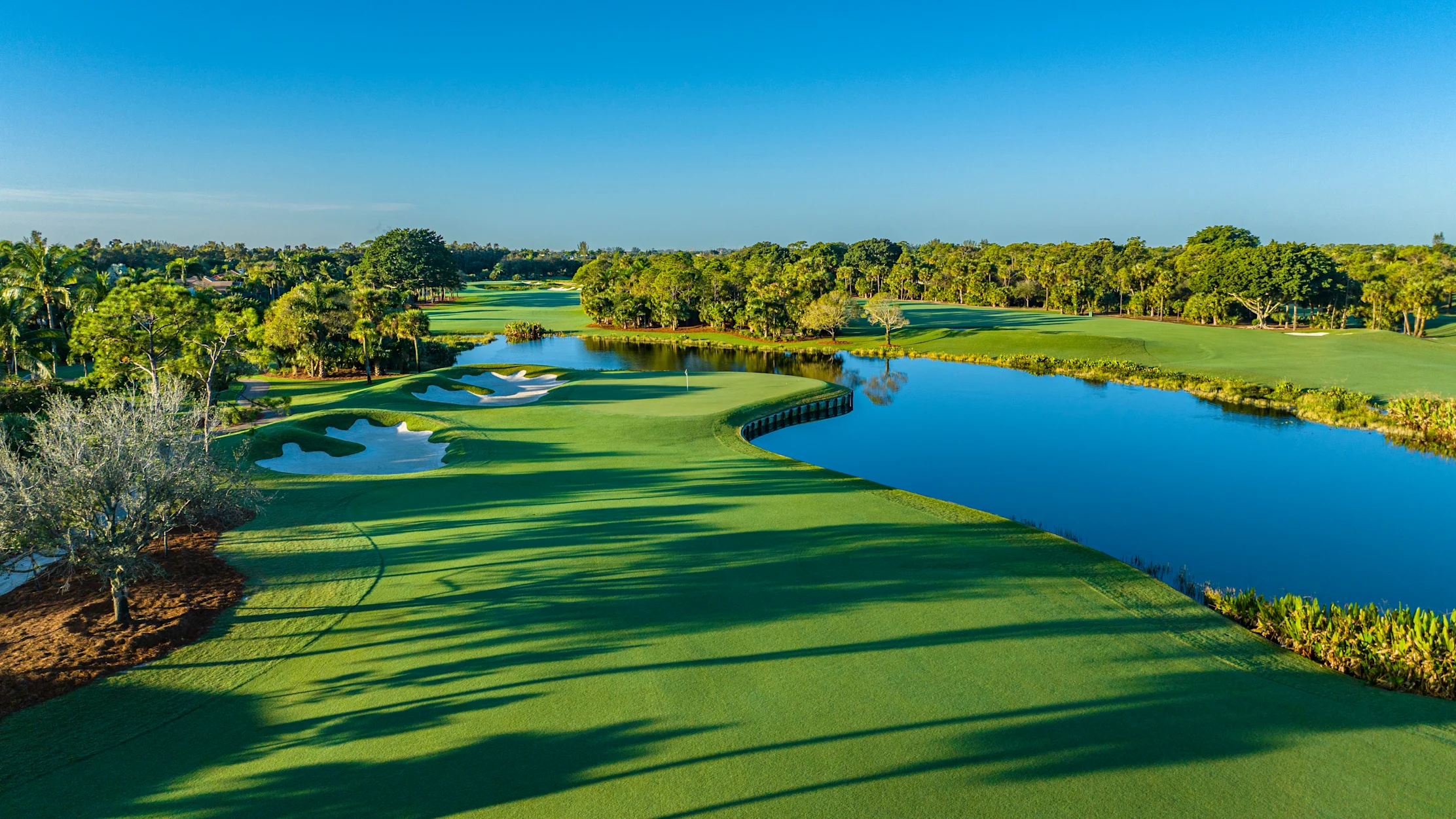 Scenic golf course with lush green fairways, blue water hazards, and trees under a clear sky.