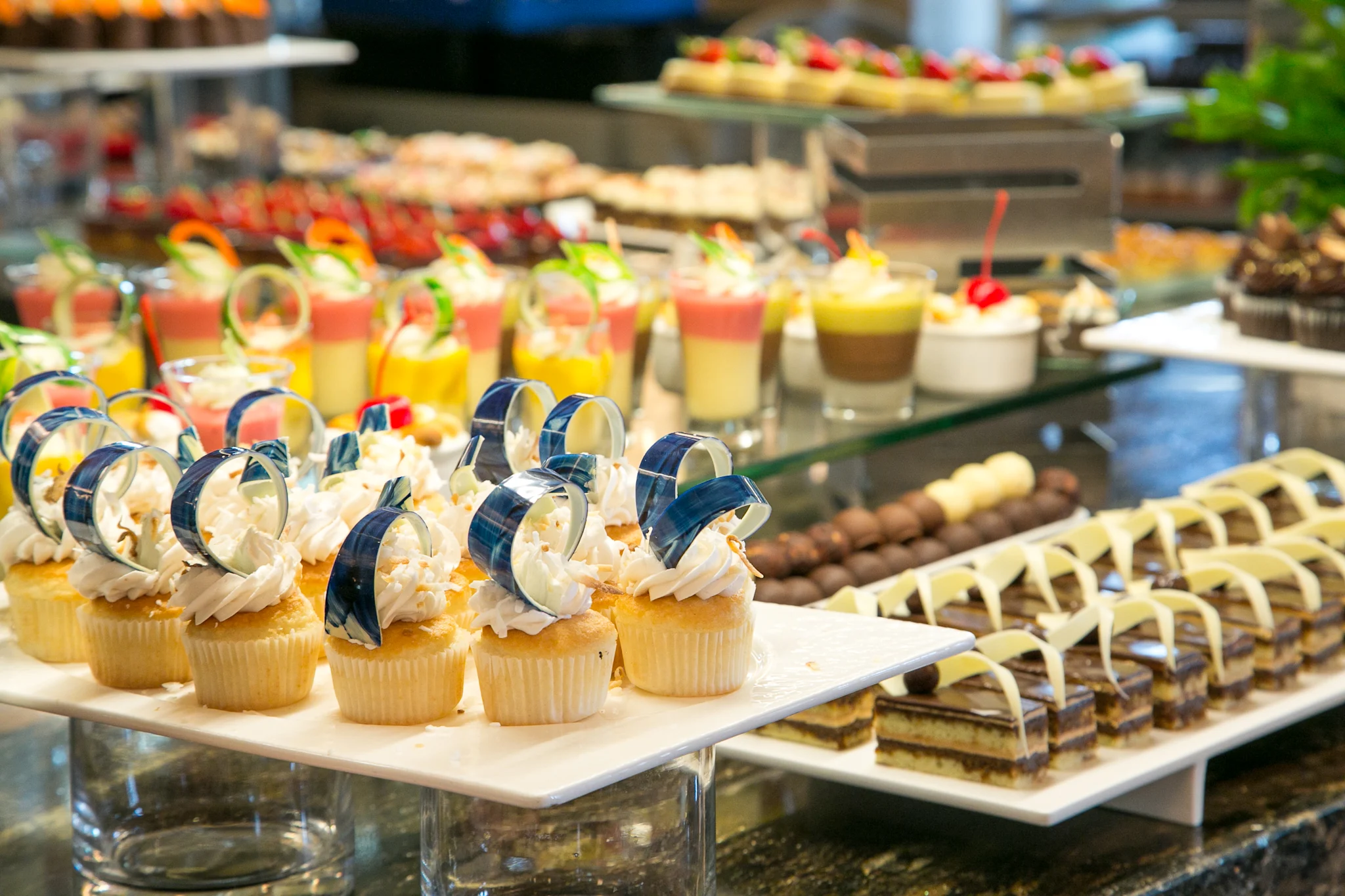 Dessert buffet display with decorated cupcakes, layered desserts, and colorful pastries on white trays.