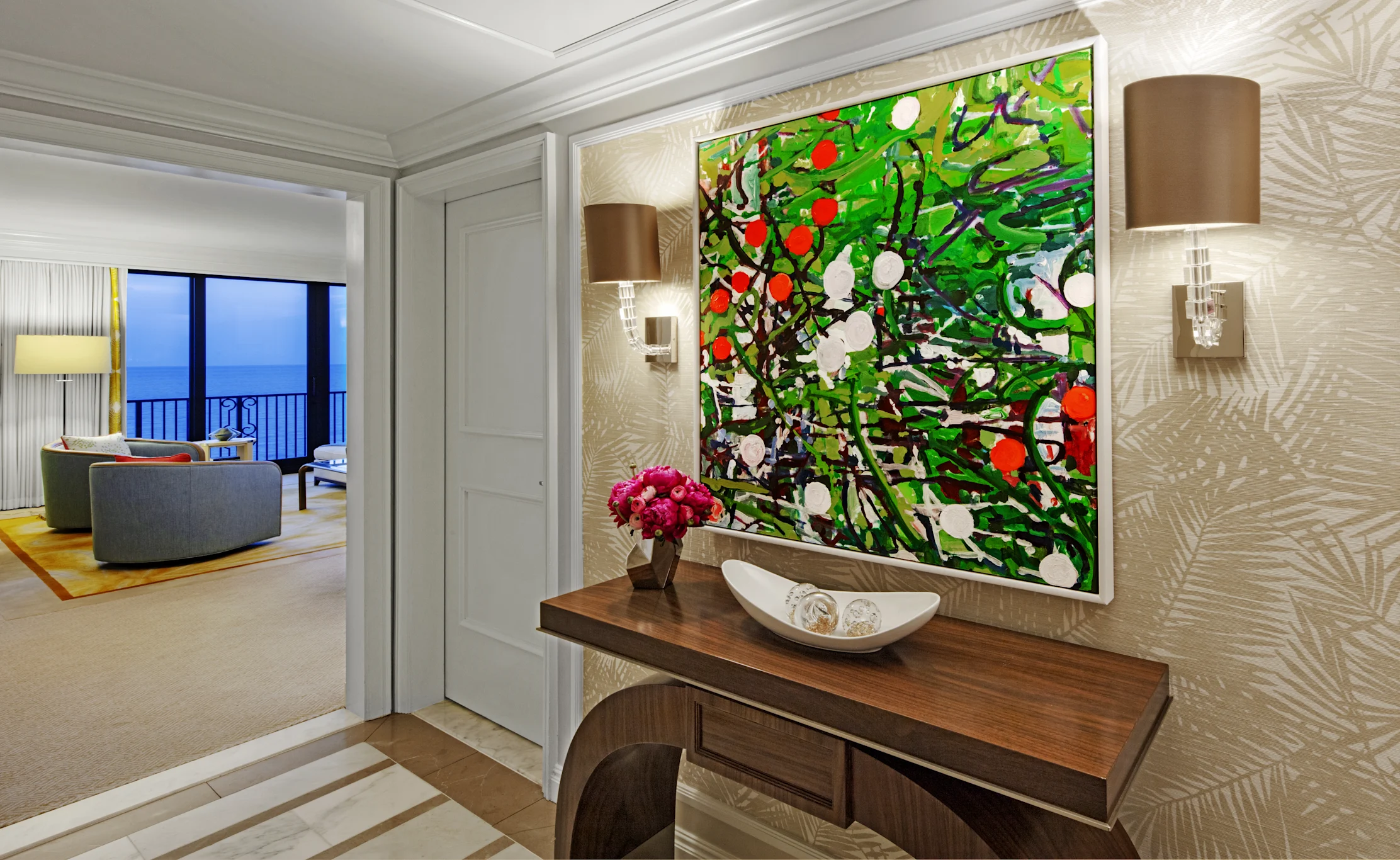 Vibrant abstract painting with green foliage and red circles above wooden console in hotel suite entryway.