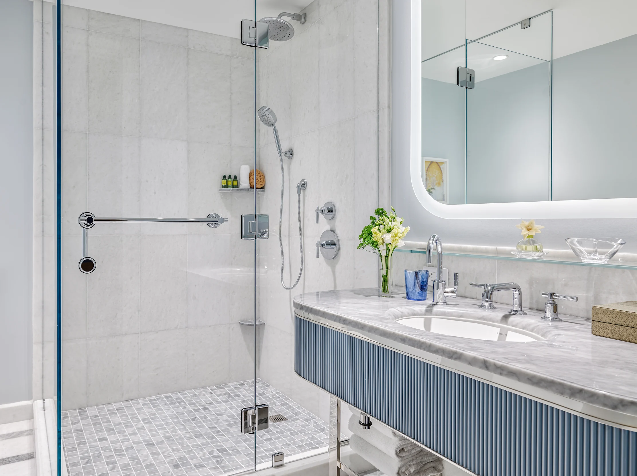Modern bathroom with glass shower, marble vanity, chrome fixtures, and white flowers on counter.